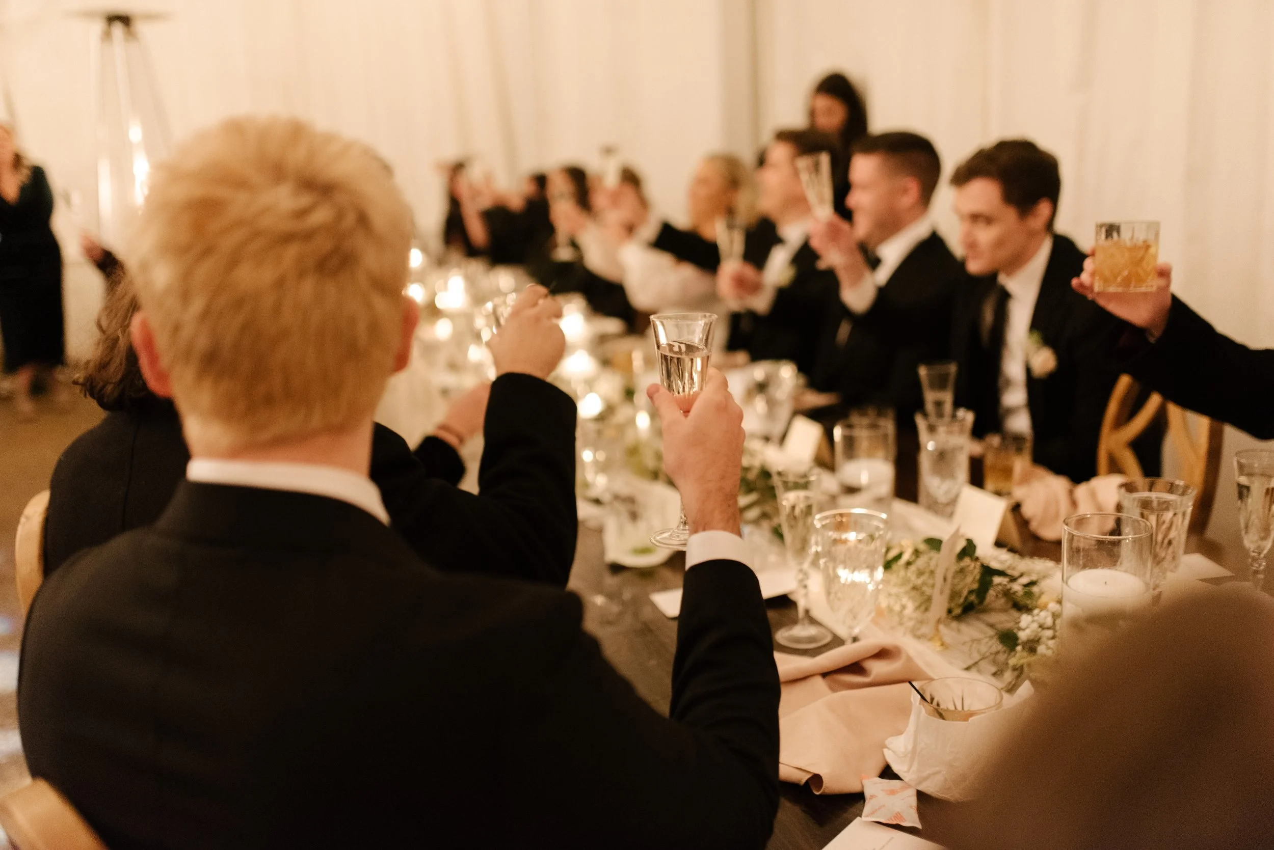 Wedding guests raising champagne glasses for a toast during an intimate reception dinner.