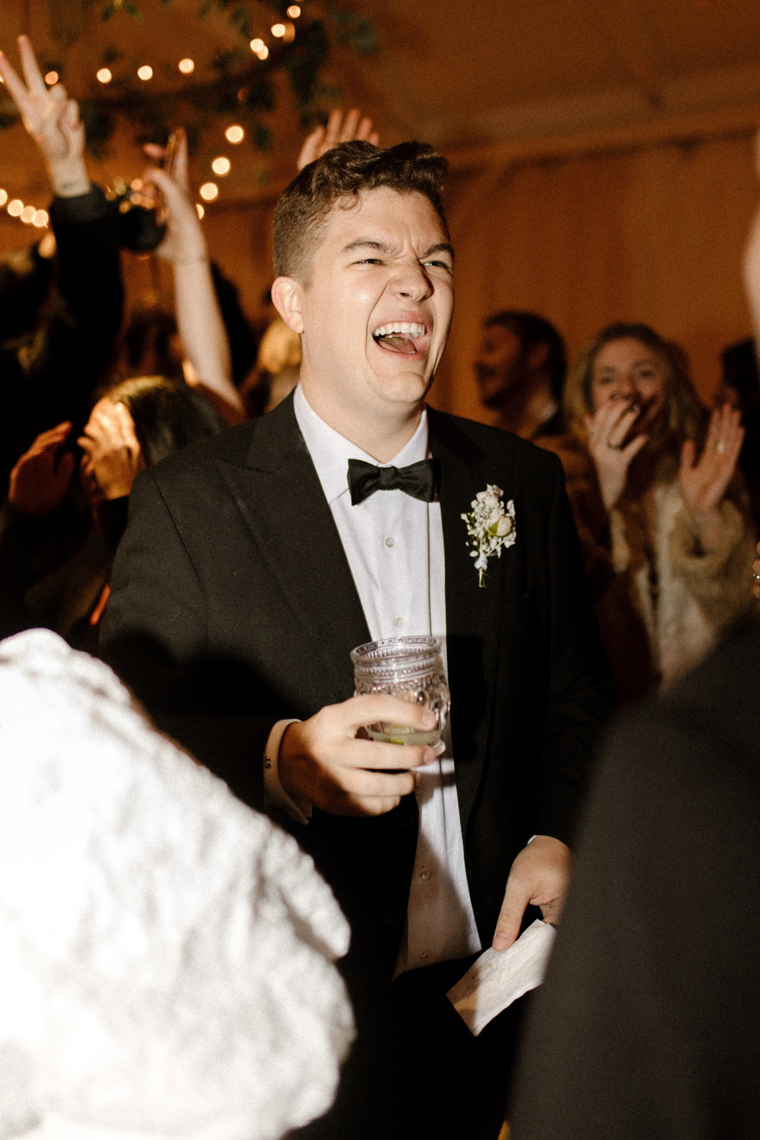 Groom laughing with a drink in hand on a crowded dance floor during a fun fall wedding reception.