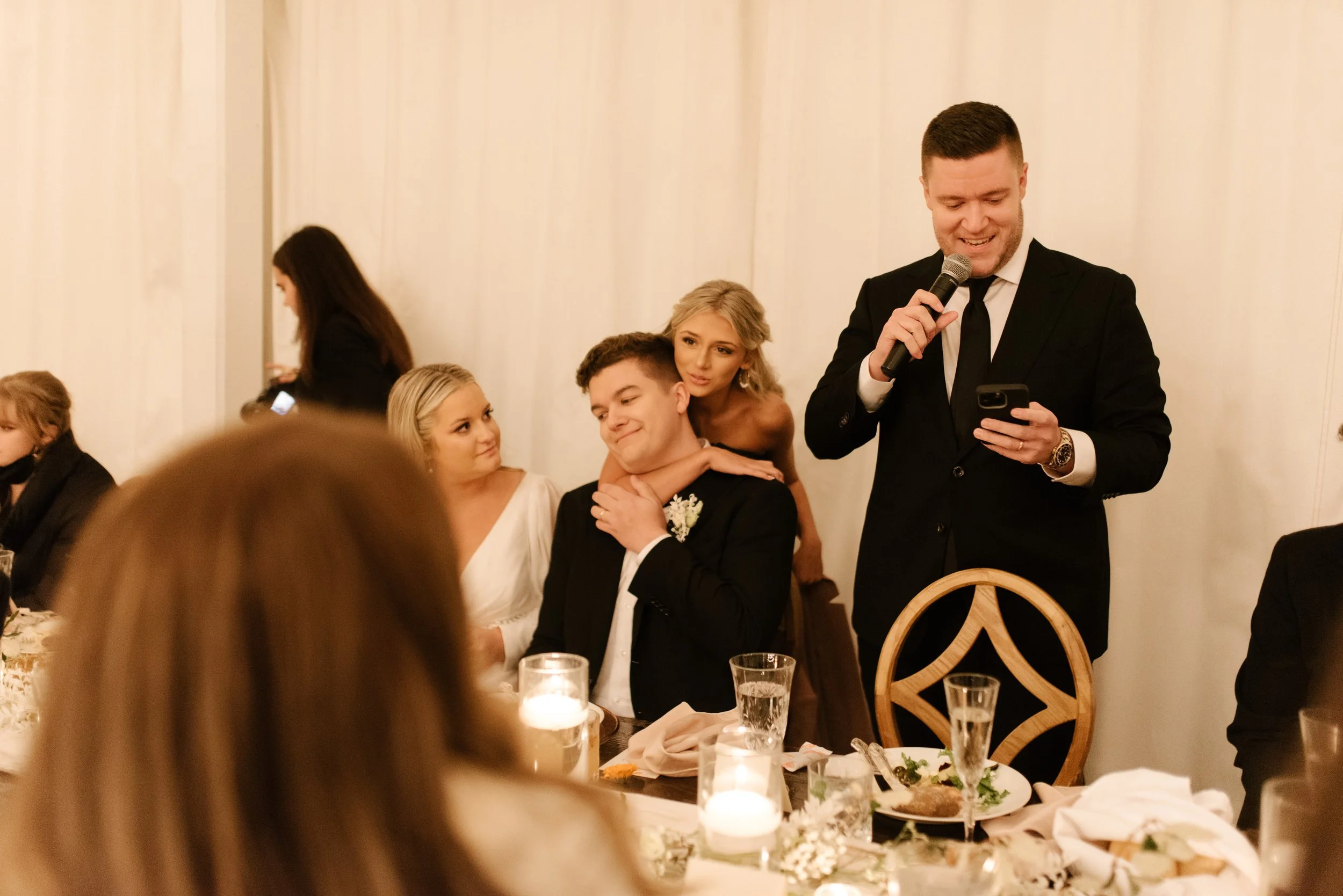 Wedding reception speech with the newlyweds laughing at their candlelit head table during a fall wedding.