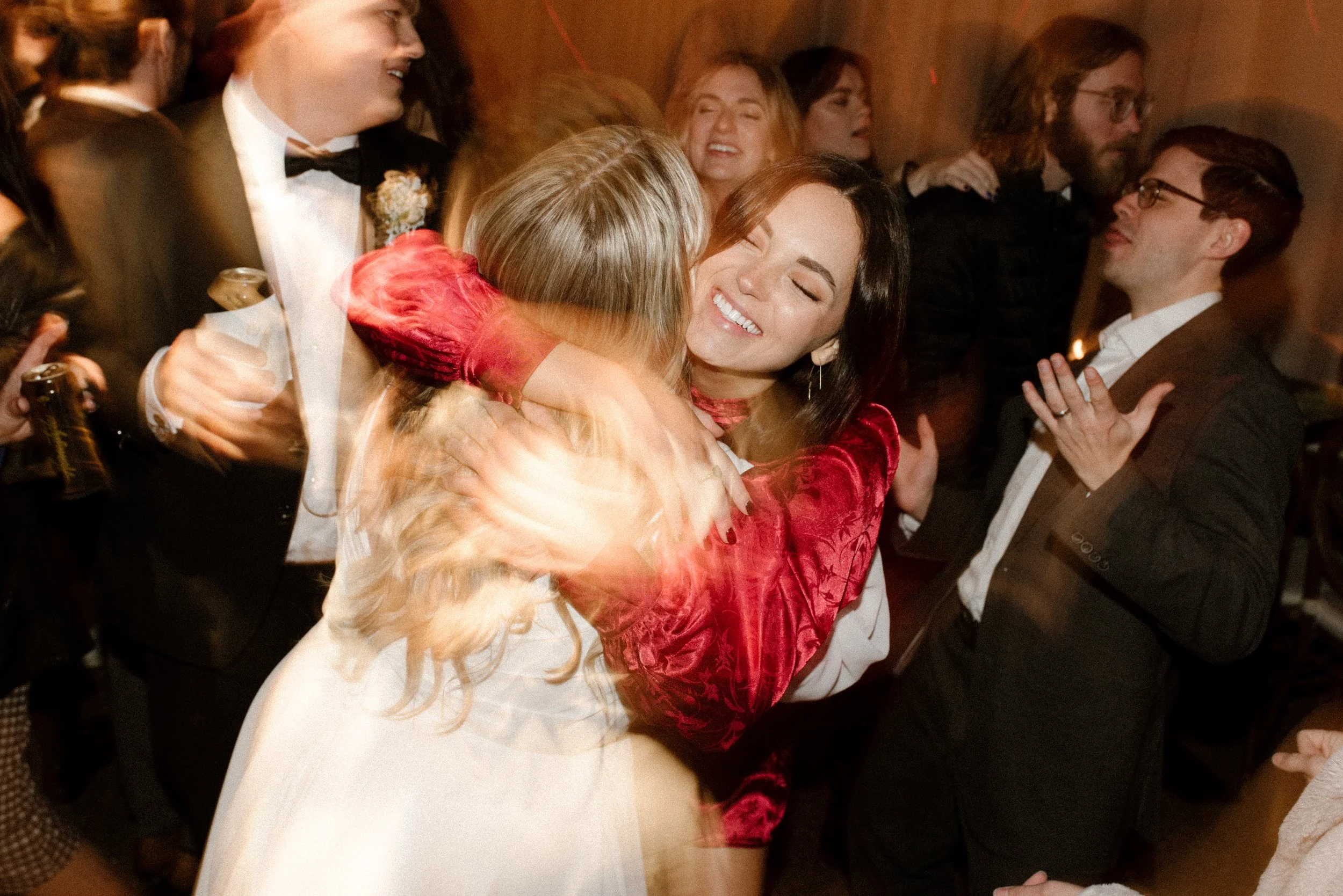 Bride hugging a friend on the dance floor during a lively fall wedding reception.