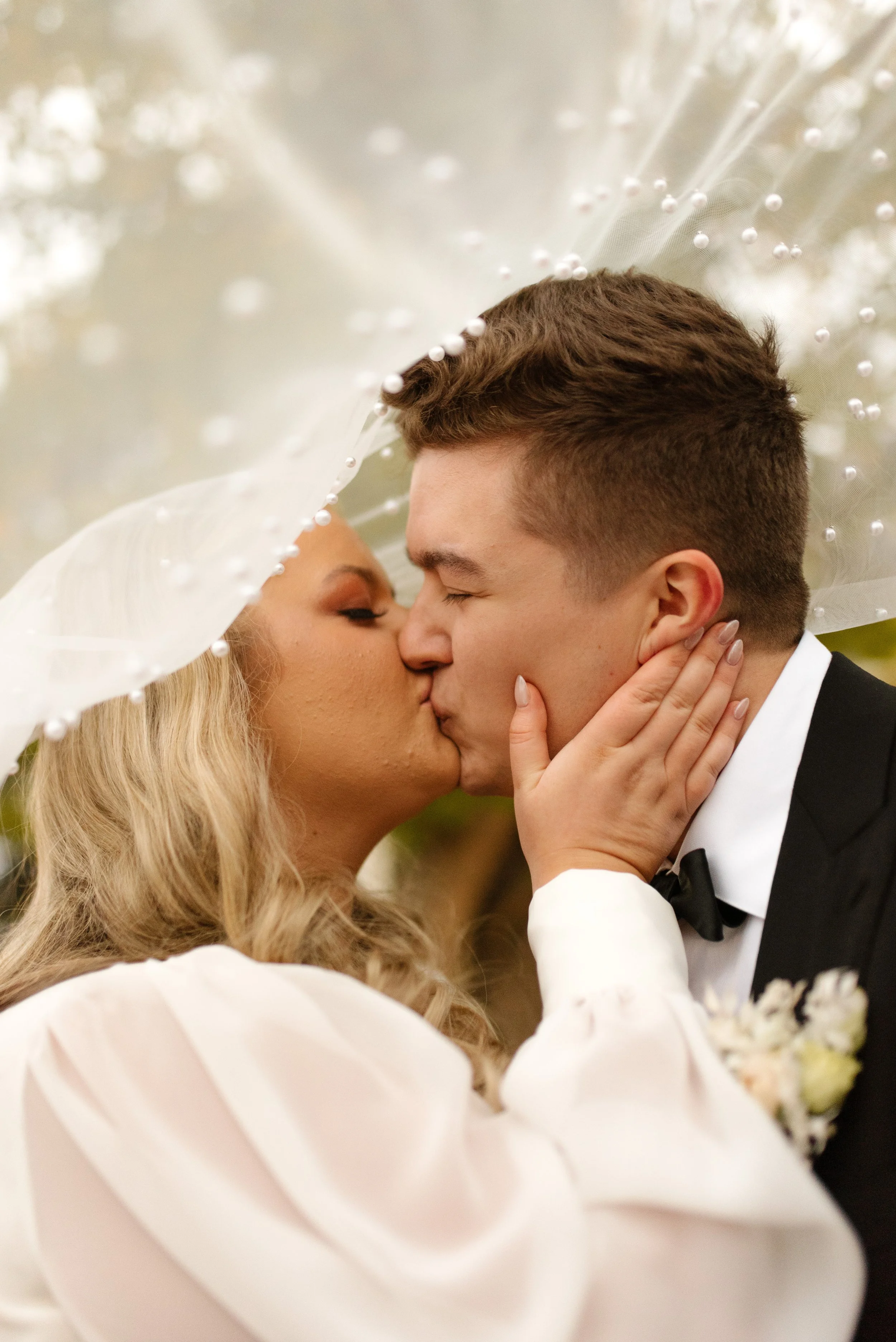 Bride and groom sharing a romantic kiss beneath her pearl-detailed veil at their fall wedding.