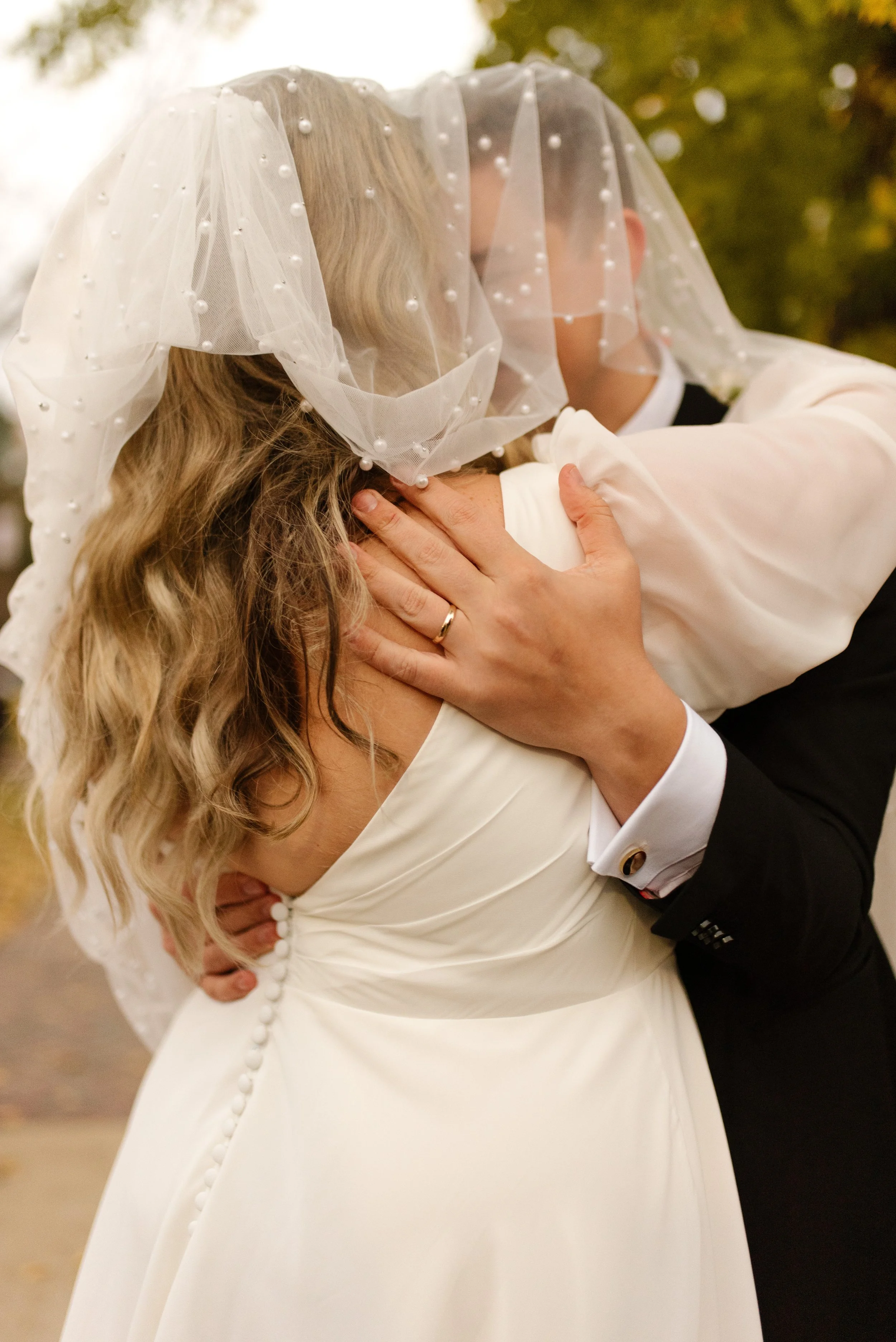 Bride and groom embracing and kissing beneath the bride's pearl-detailed veil.