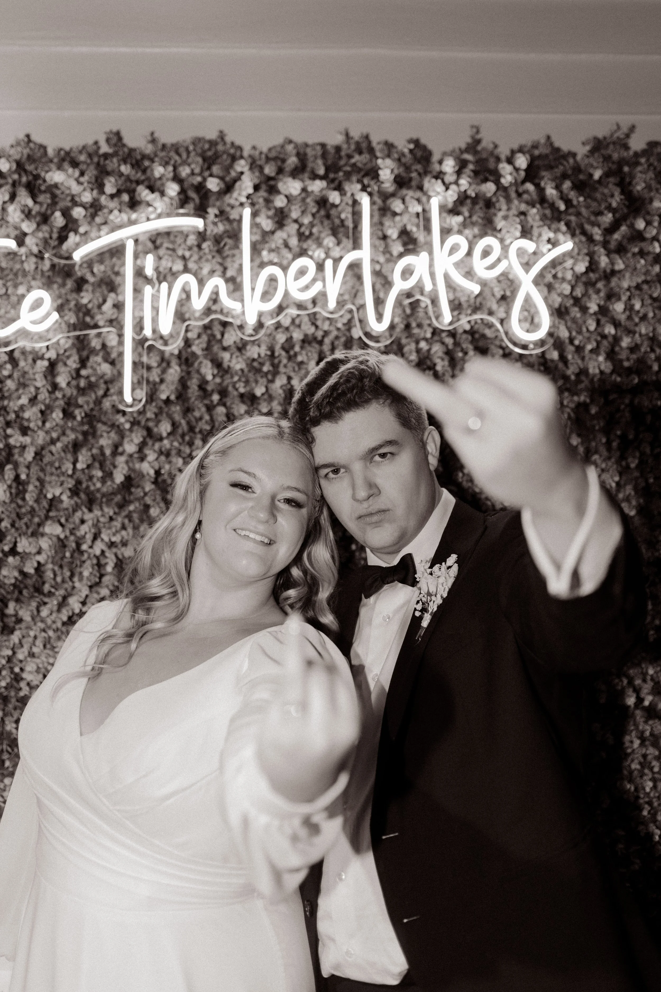 Newlyweds posing playfully in front of a floral photo backdrop during their fall wedding reception.