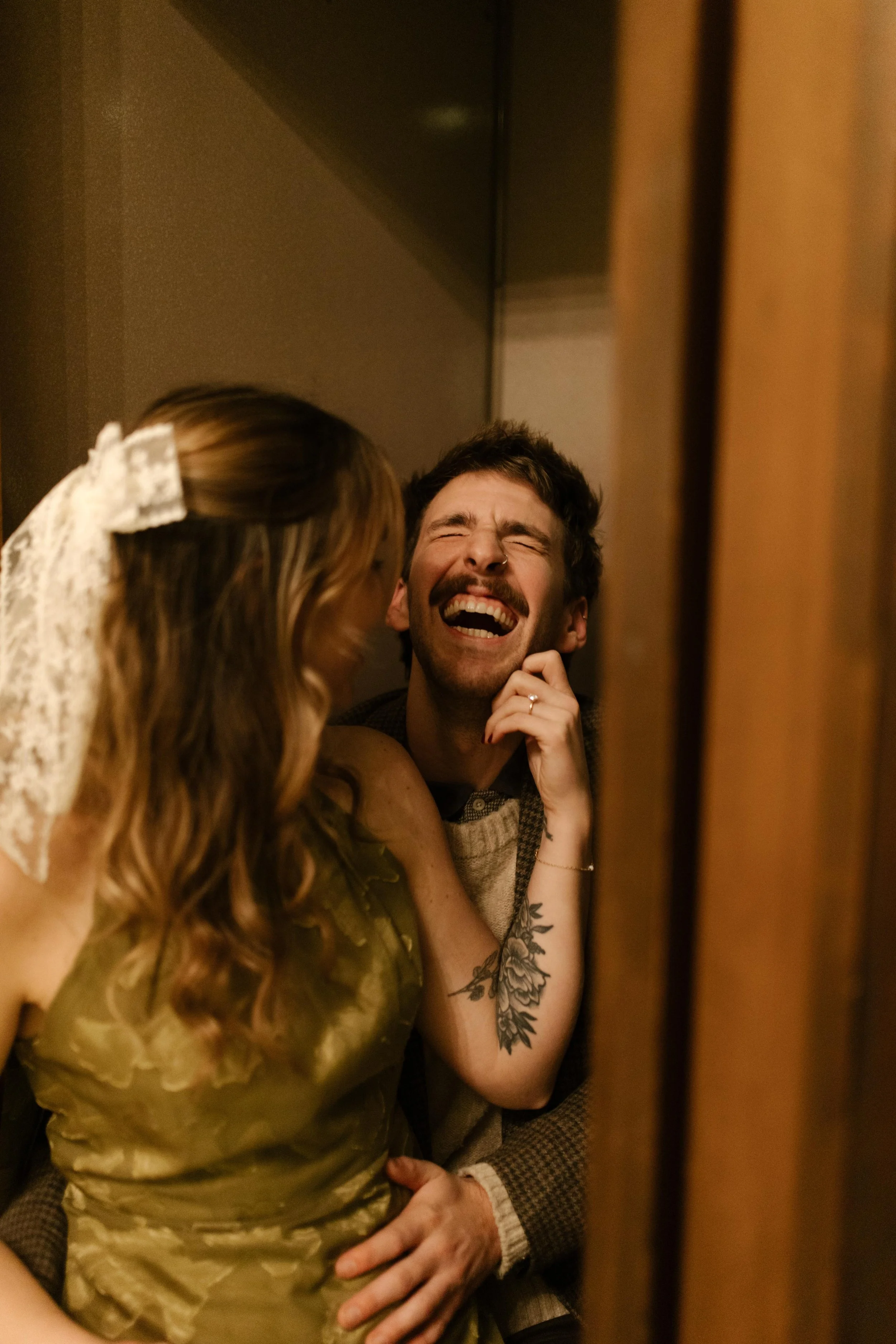 Playful candid portrait of an engaged couple laughing together in a vintage wood-paneled booth.
