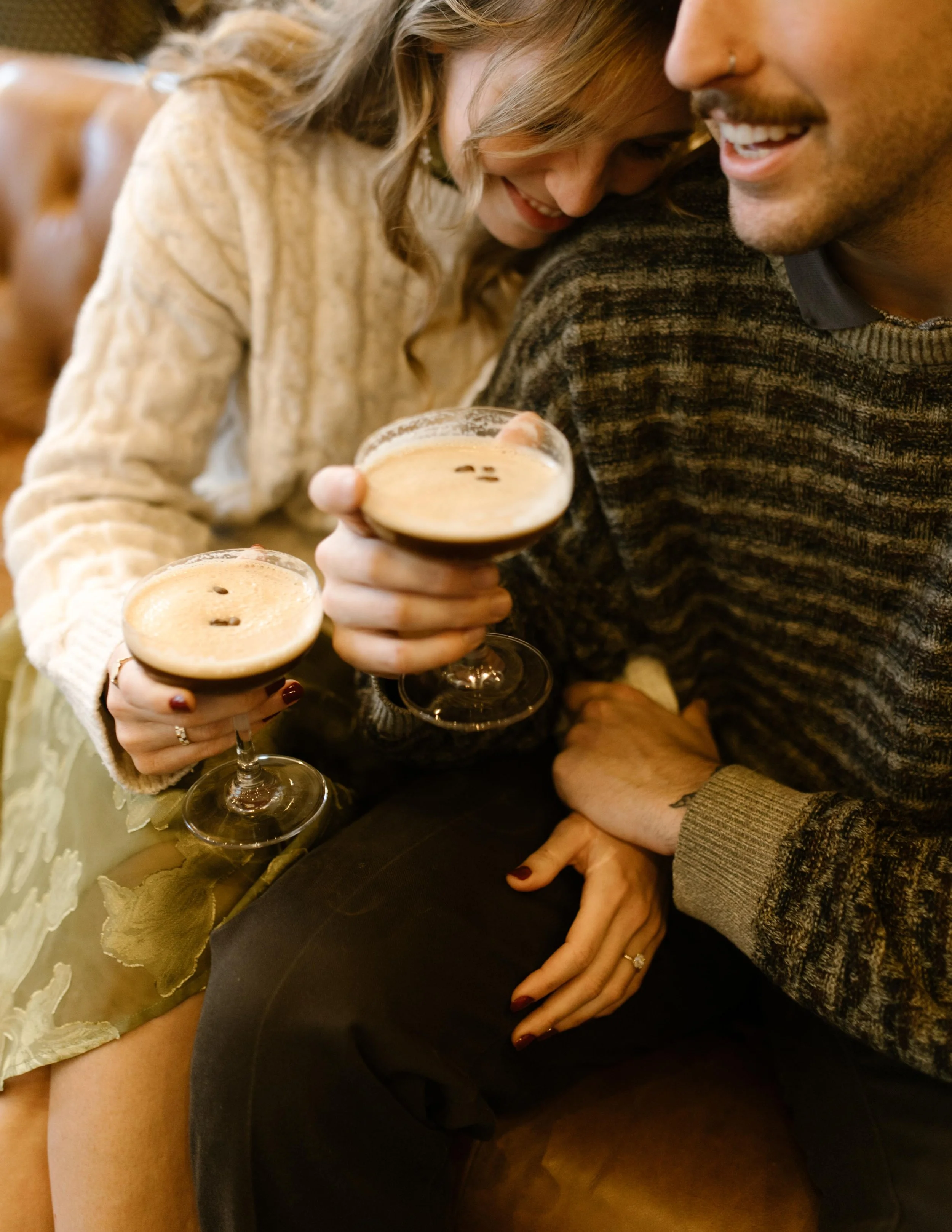 Couple cuddling with espresso martinis during engagement photos in NYC, with the engagement ring visible on her hand.