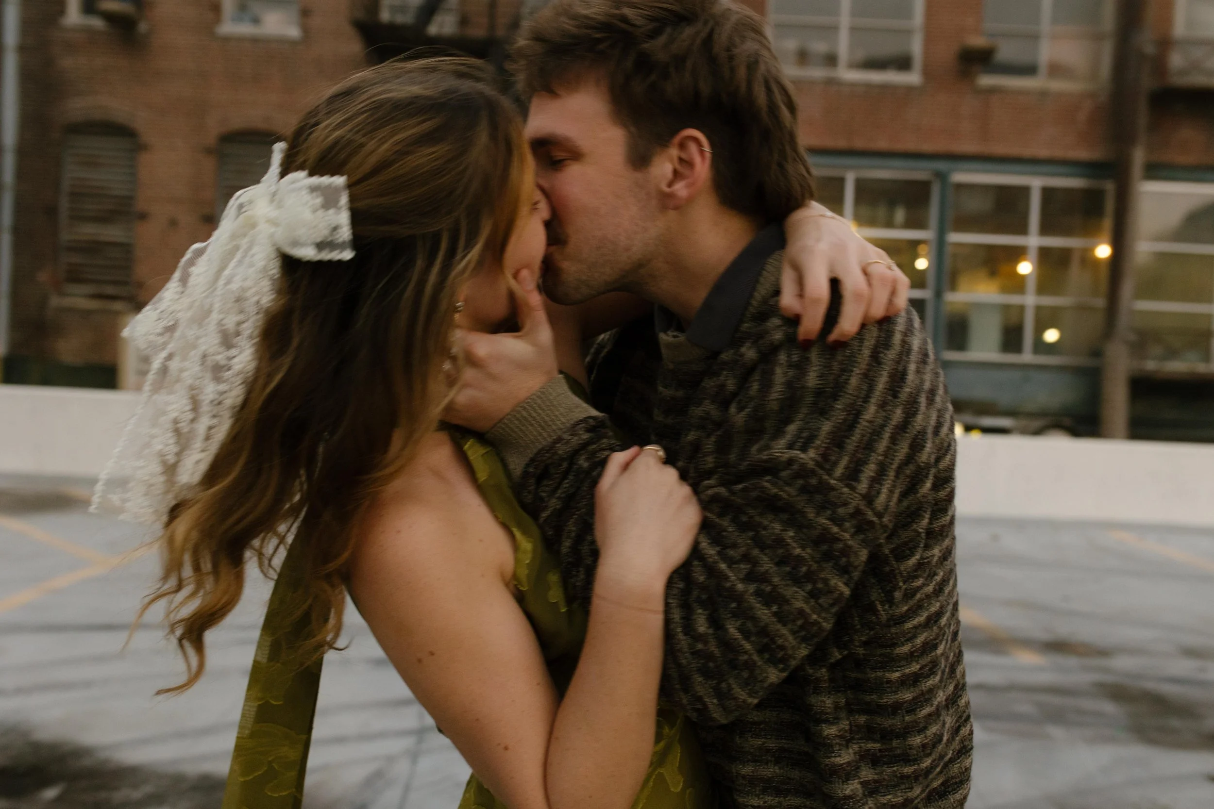 Close-up of an engaged couple kissing on a rooftop during a playful city photo session.