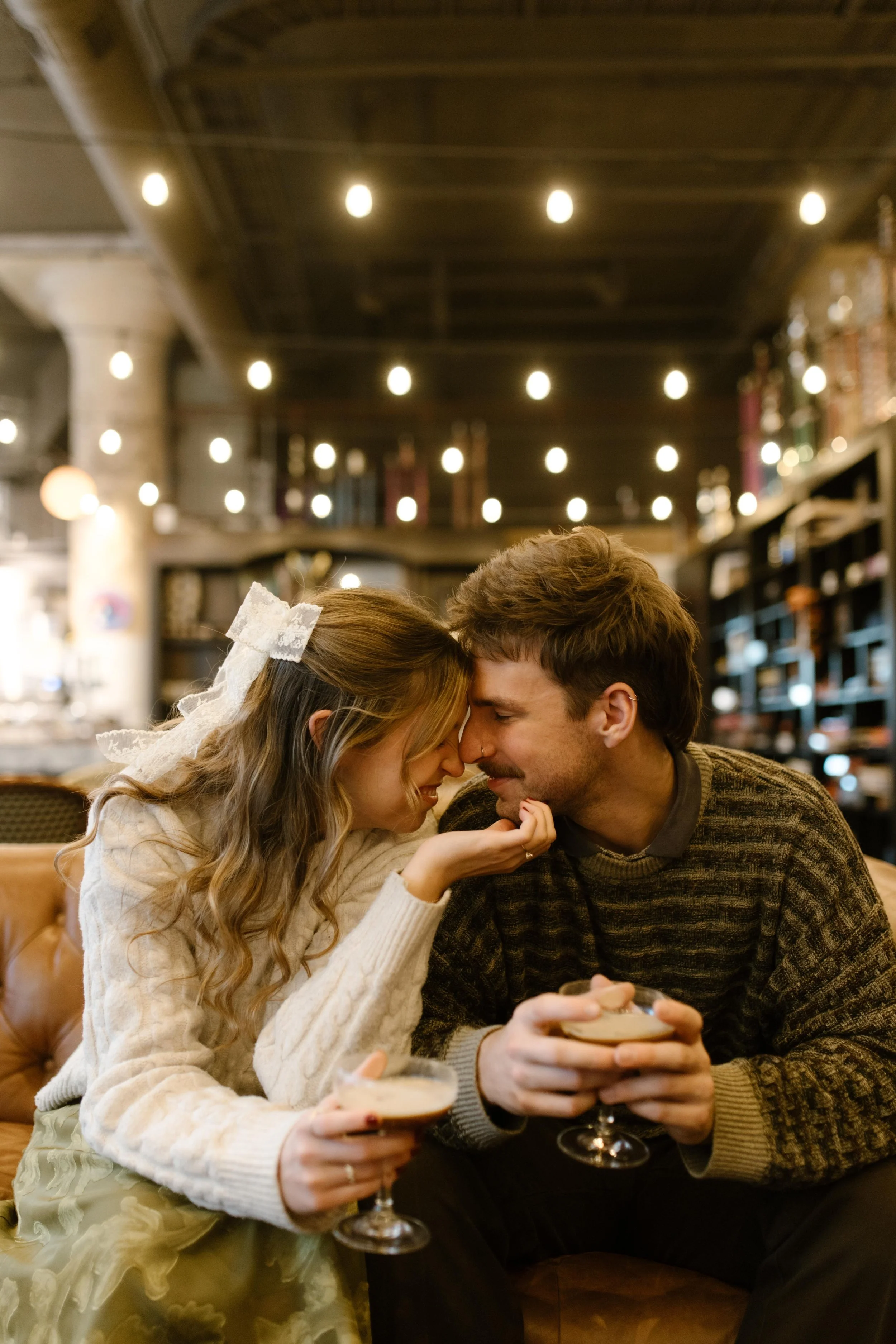 Couple touching foreheads while enjoying cocktails together in a warmly lit lounge.