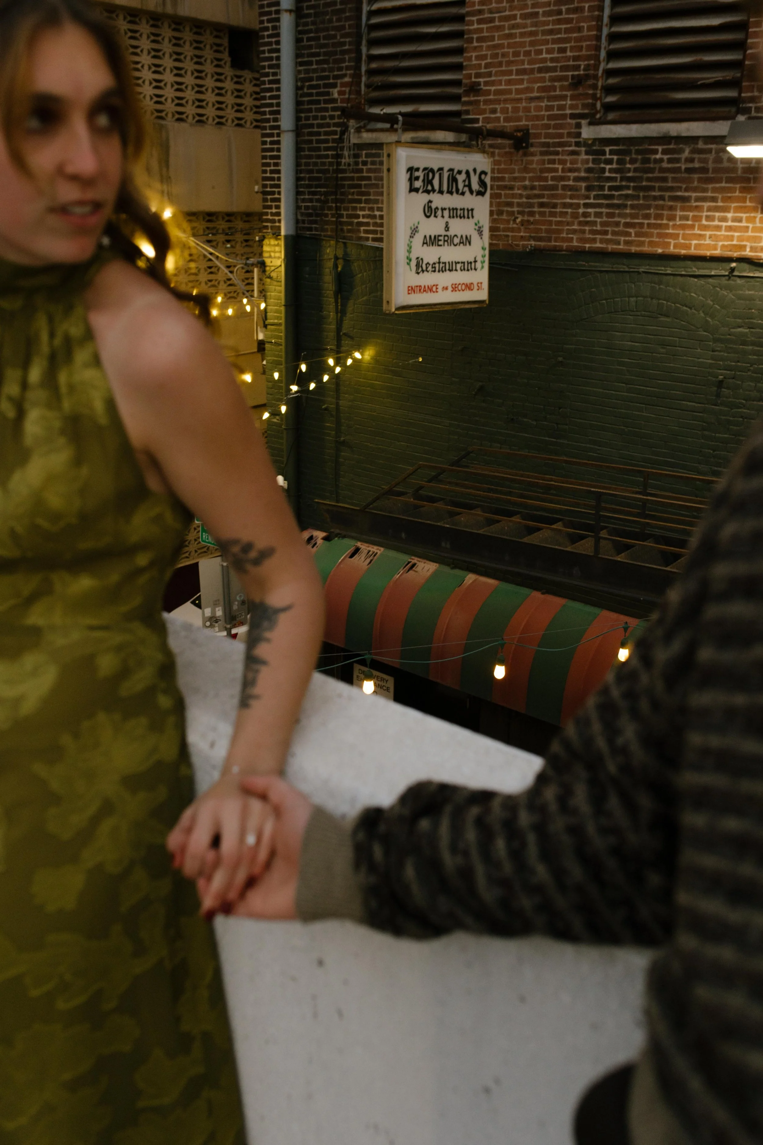 Engaged couple holding hands during engagement photos in NYC near a vintage restaurant sign and string lights.