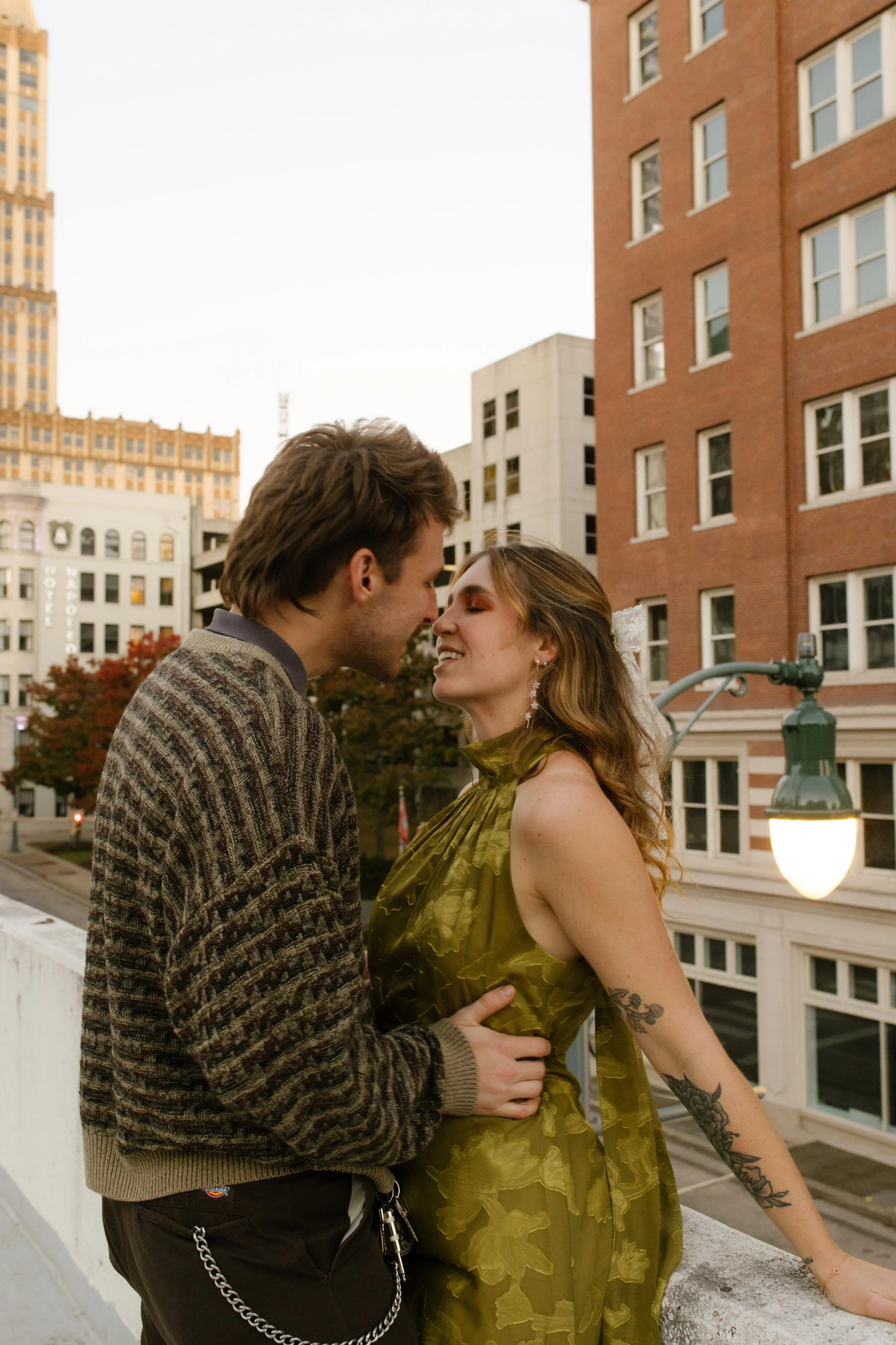 Couple leaning in for a kiss during engagement photos in NYC with downtown buildings and a glowing streetlamp behind them.
