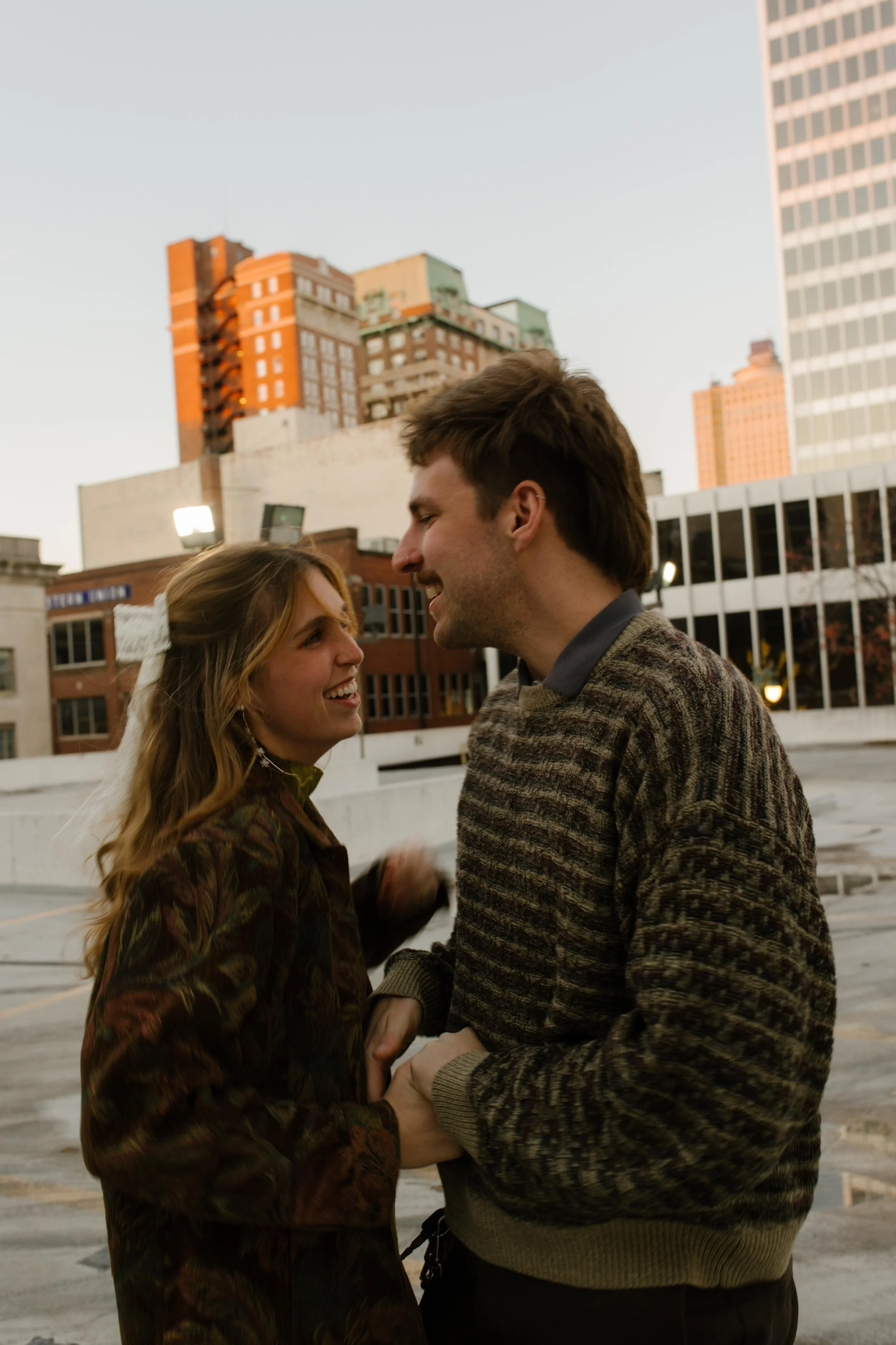 Couple laughing and holding hands on a rooftop during engagement photos in NYC, surrounded by downtown buildings.