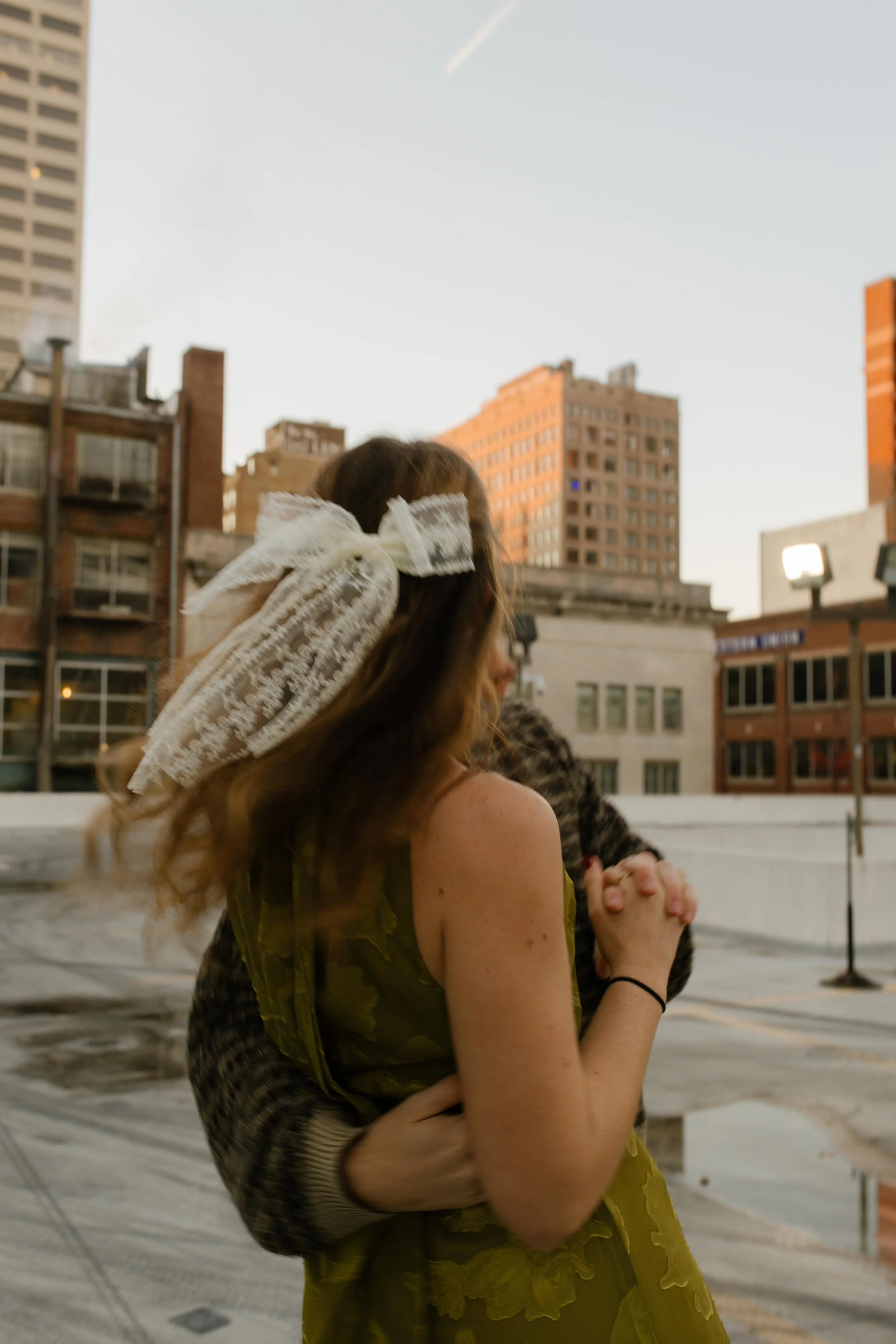 Engaged couple dancing together on a rooftop with her lace hair bow flowing behind her.