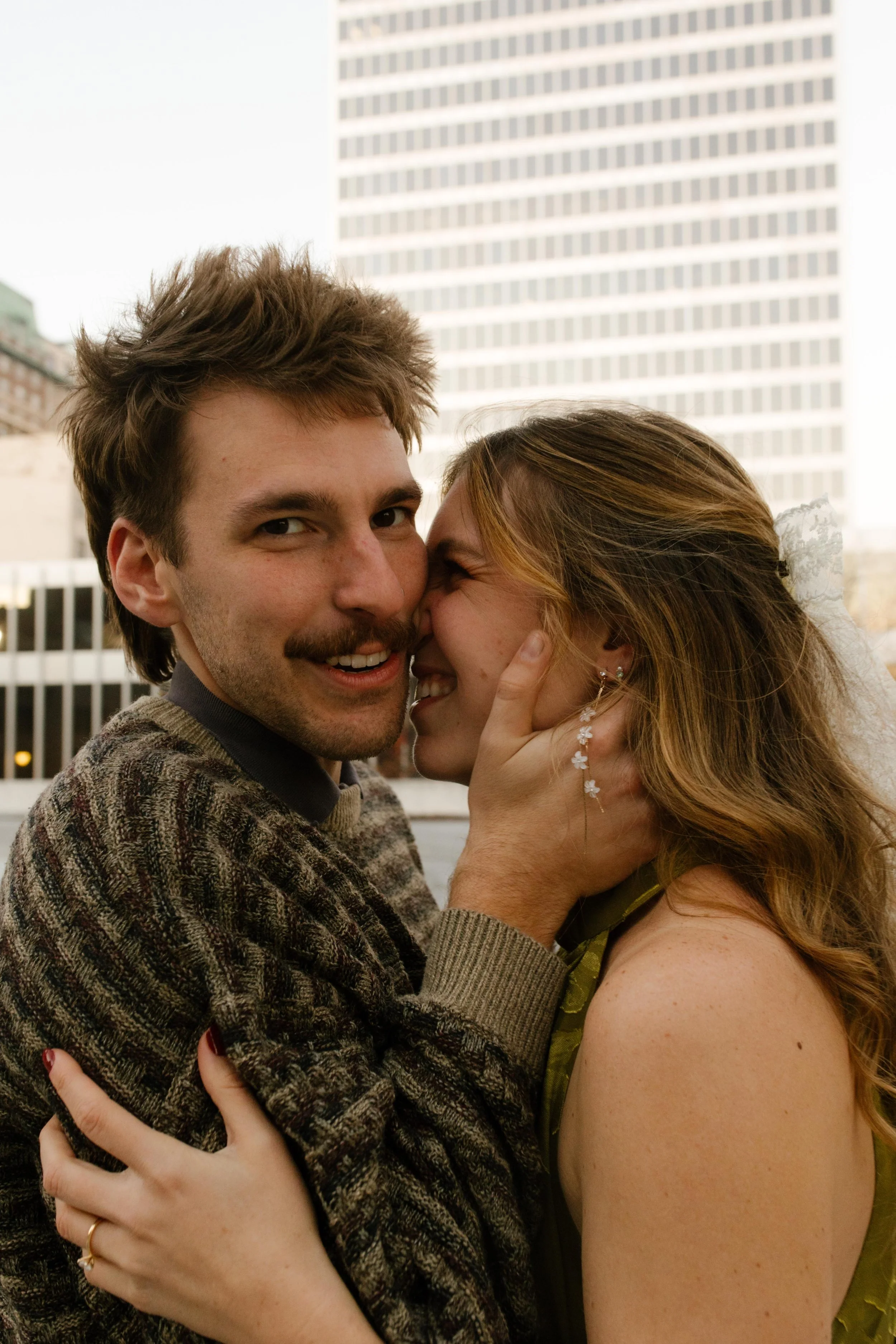 Playful close-up from engagement photos in NYC as the couple cuddles and laughs with the city skyline behind them.