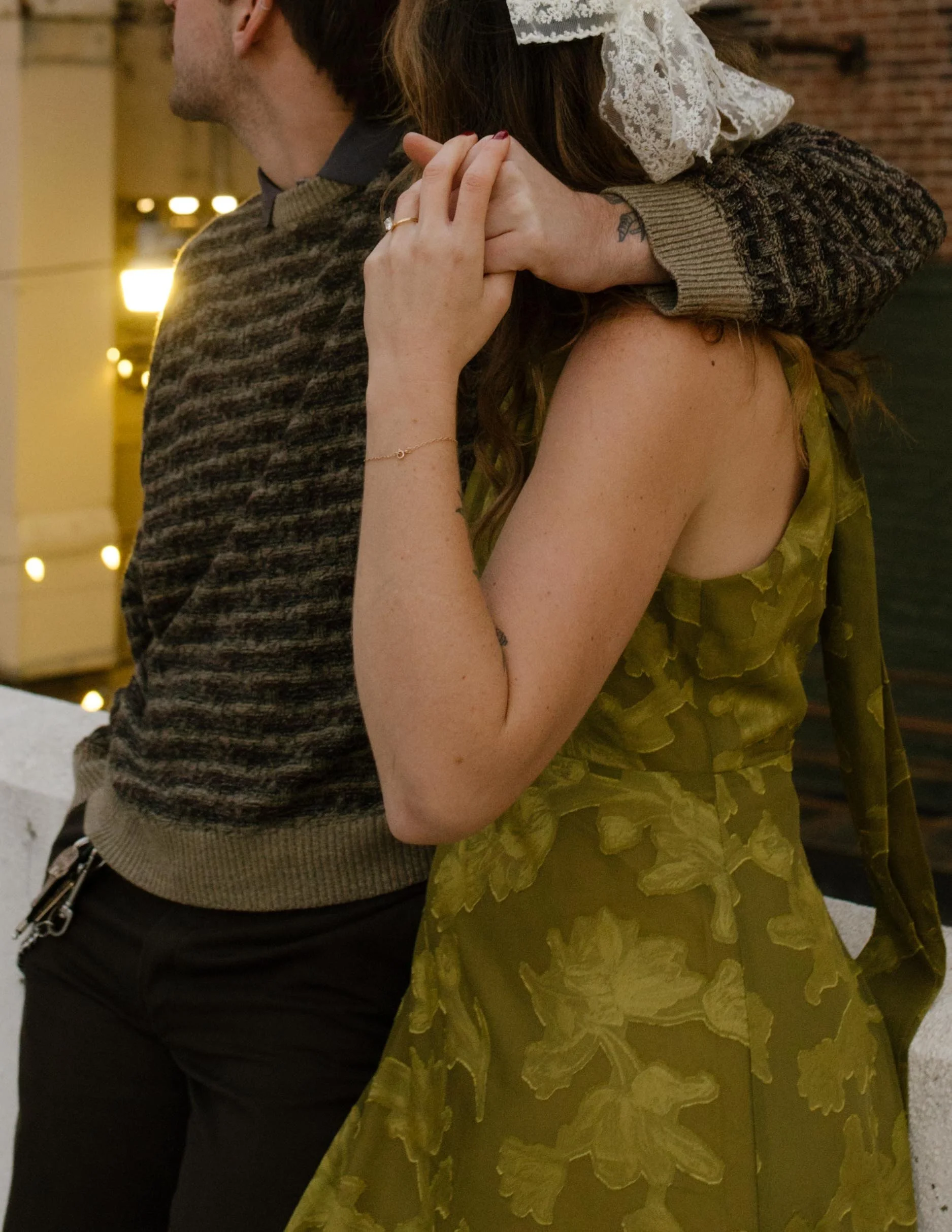 1. Close-up of an engaged couple holding hands while embracing, highlighting her green floral dress and lace hair bow.