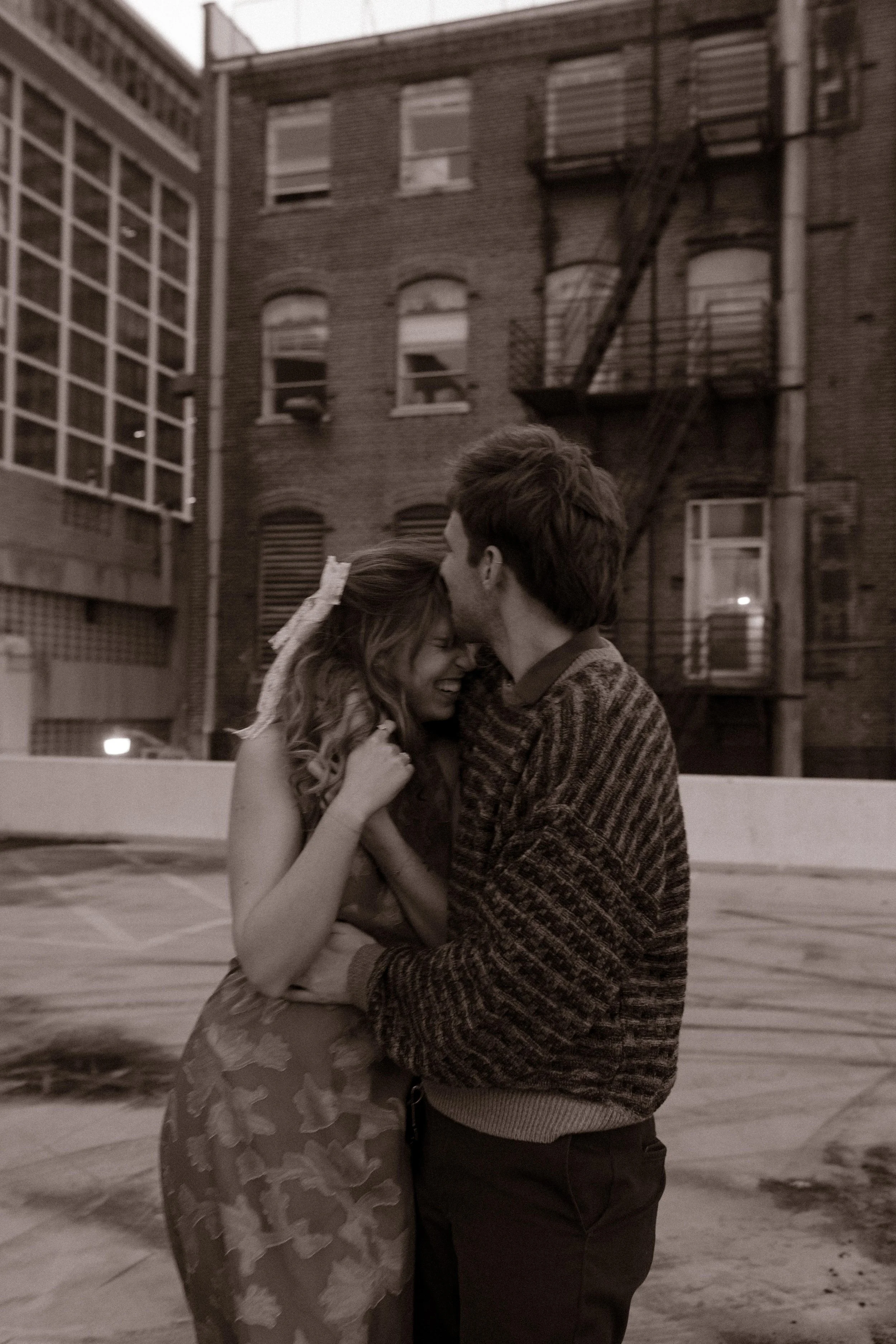 Black-and-white portrait from engagement photos in NYC of a couple embracing on a rooftop surrounded by brick buildings.