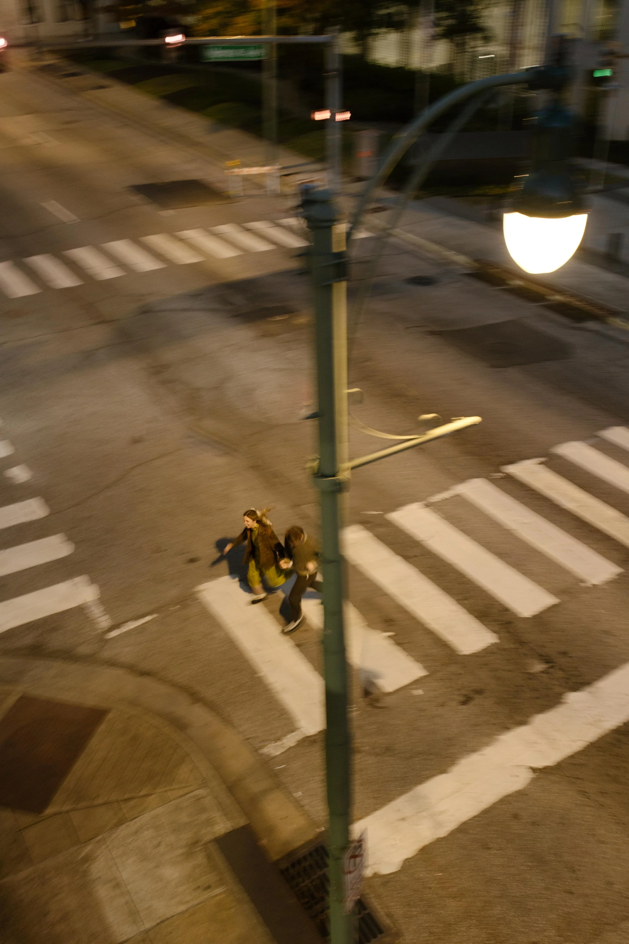Candid overhead view of an engaged couple walking together through a city crosswalk at dusk.