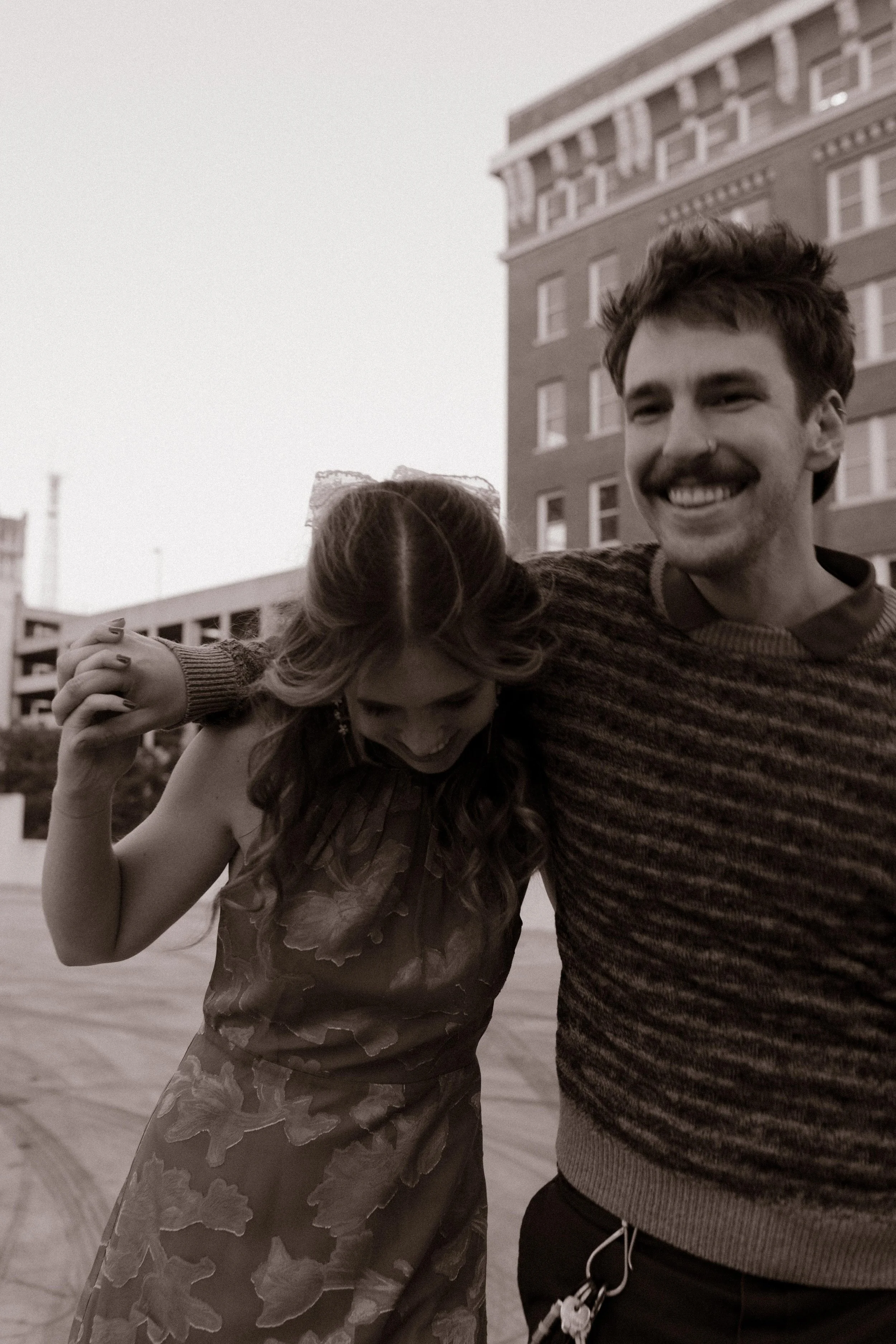 Black-and-white candid of an engaged couple walking arm in arm and laughing during engagement photos in NYC.