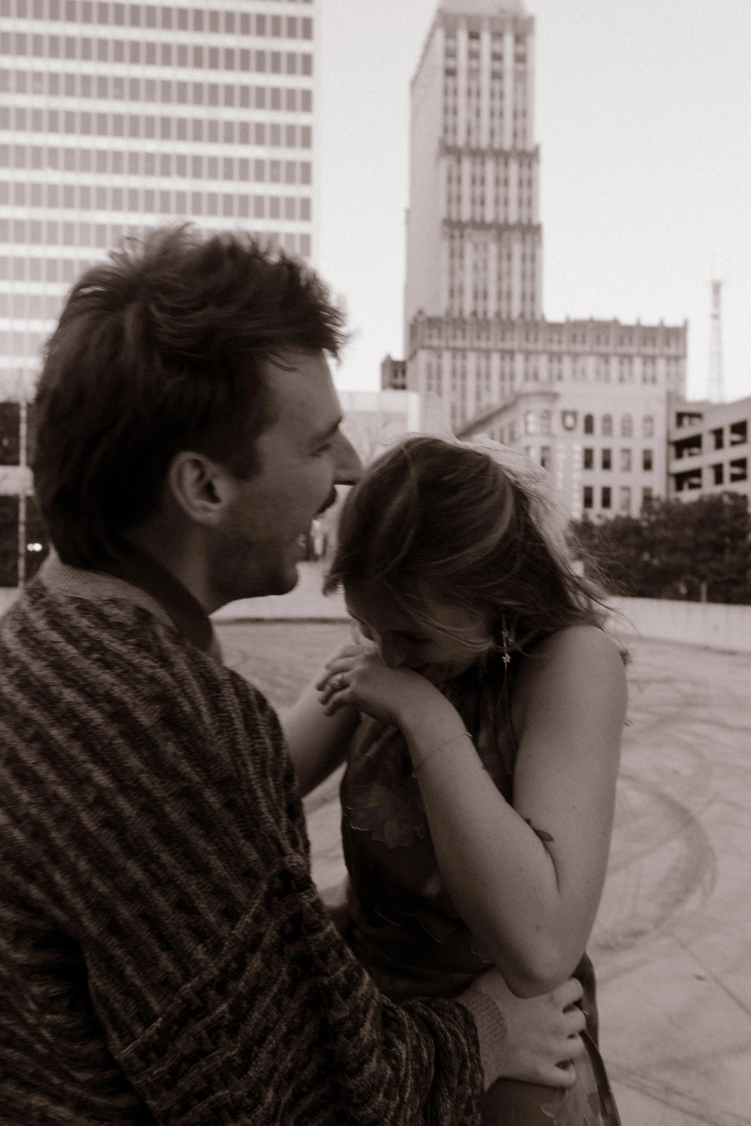 Black-and-white candid of an engaged couple laughing together during a playful rooftop photo session.