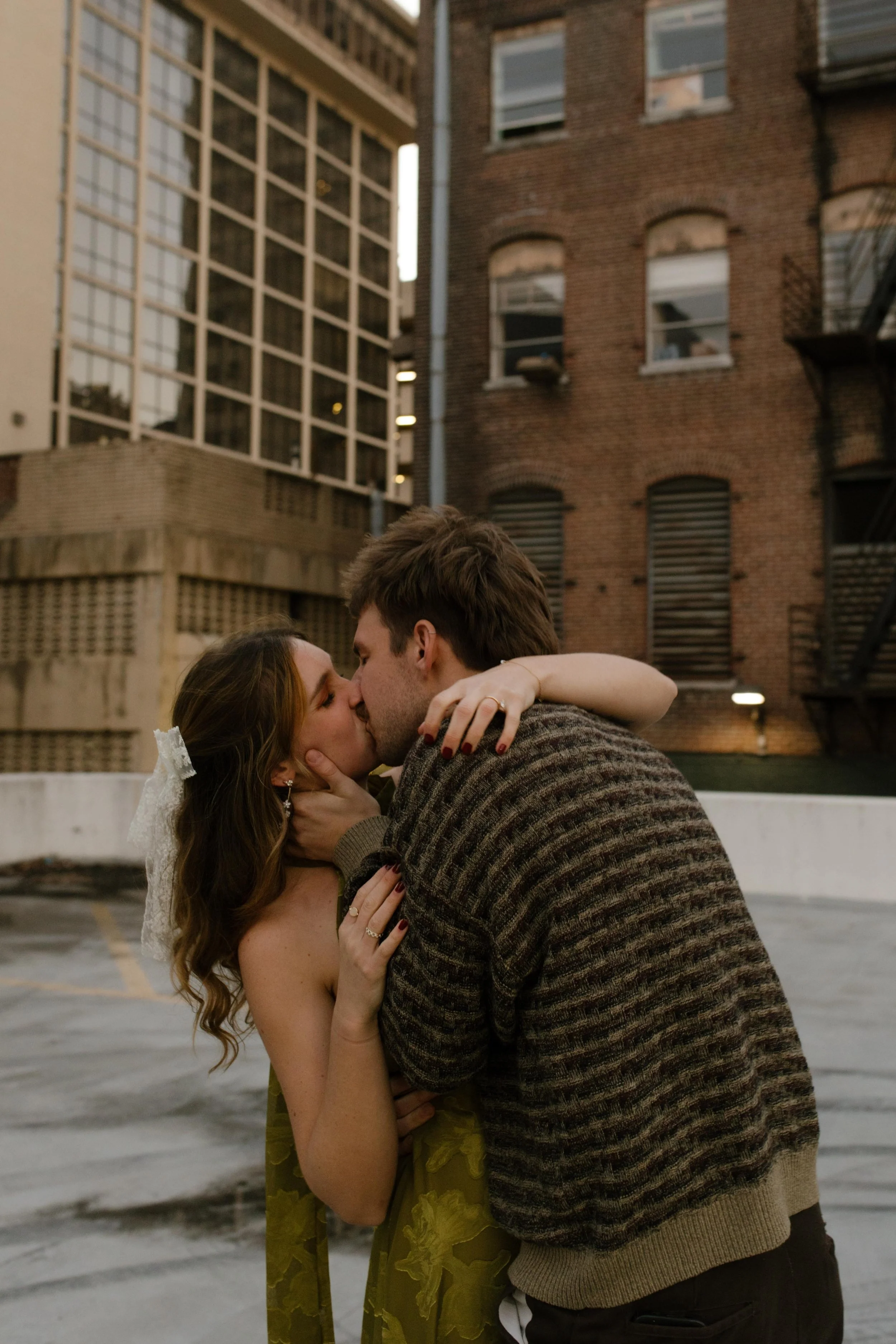 Couple kissing on a rooftop during engagement photos in NYC, framed by brick buildings and city architecture.