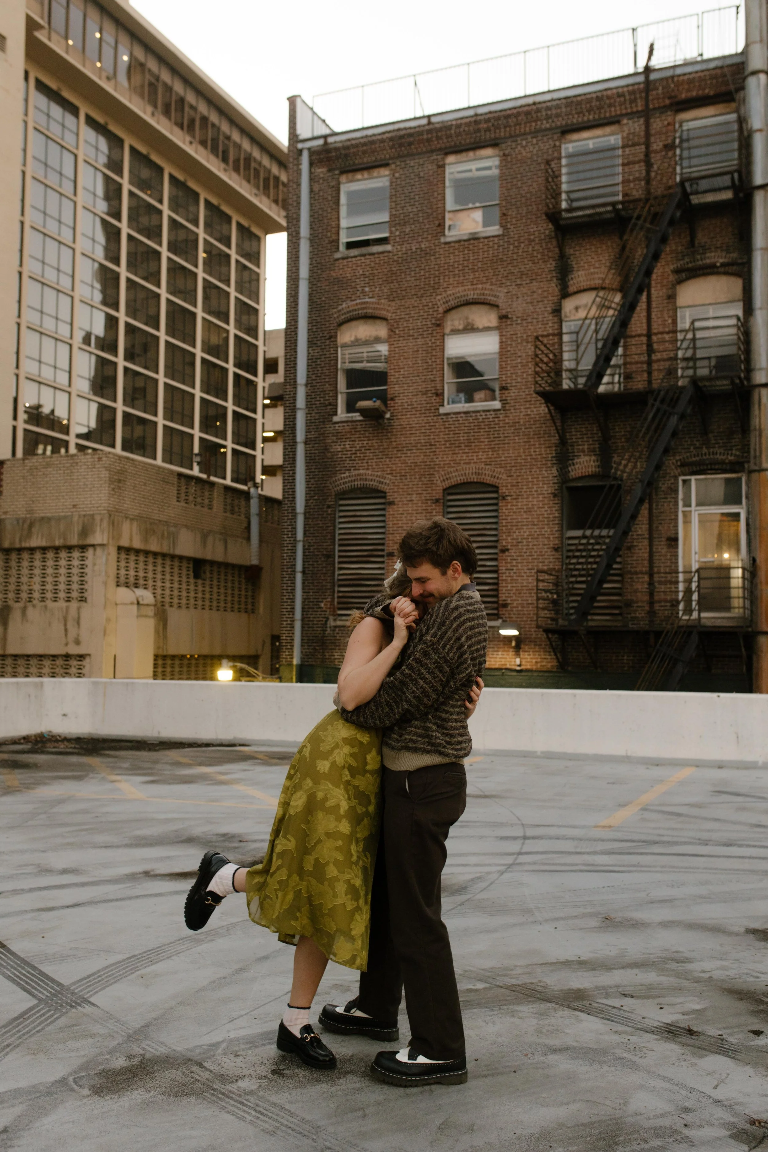 Engaged couple hugging on a rooftop during engagement photos in NYC, with a brick building and fire escape behind them.