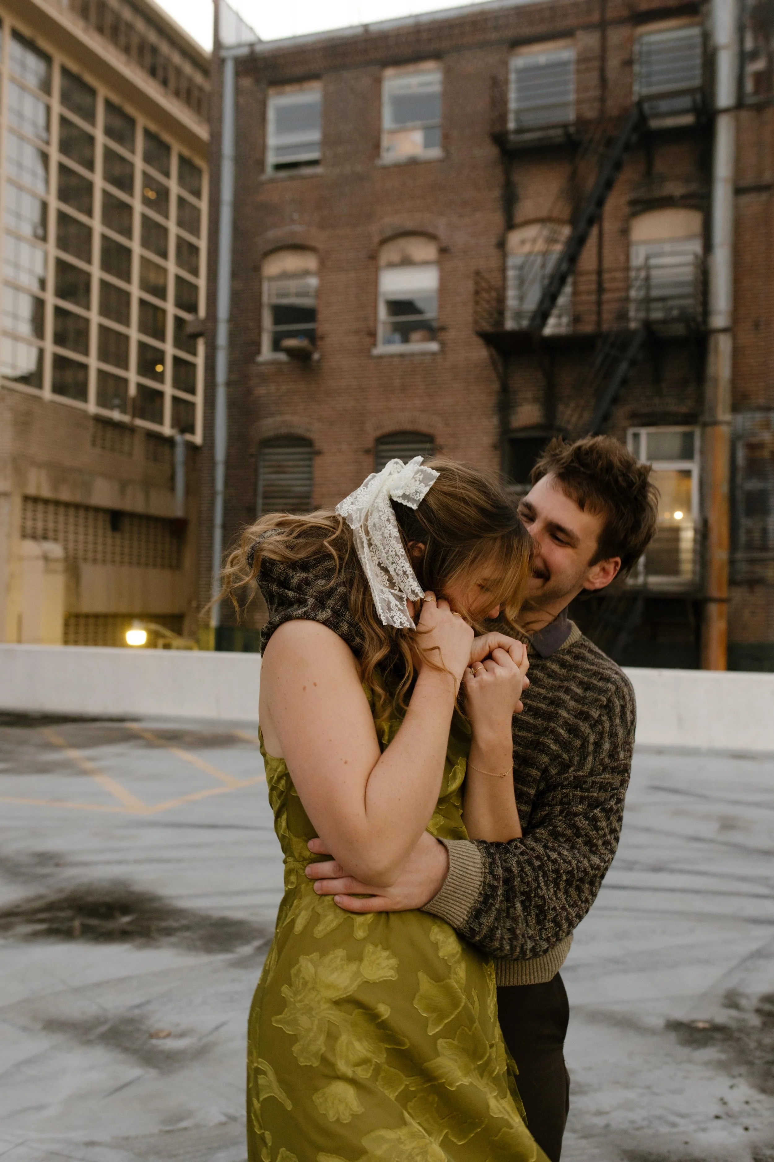 Engaged couple cuddling and laughing together during a playful rooftop portrait session.