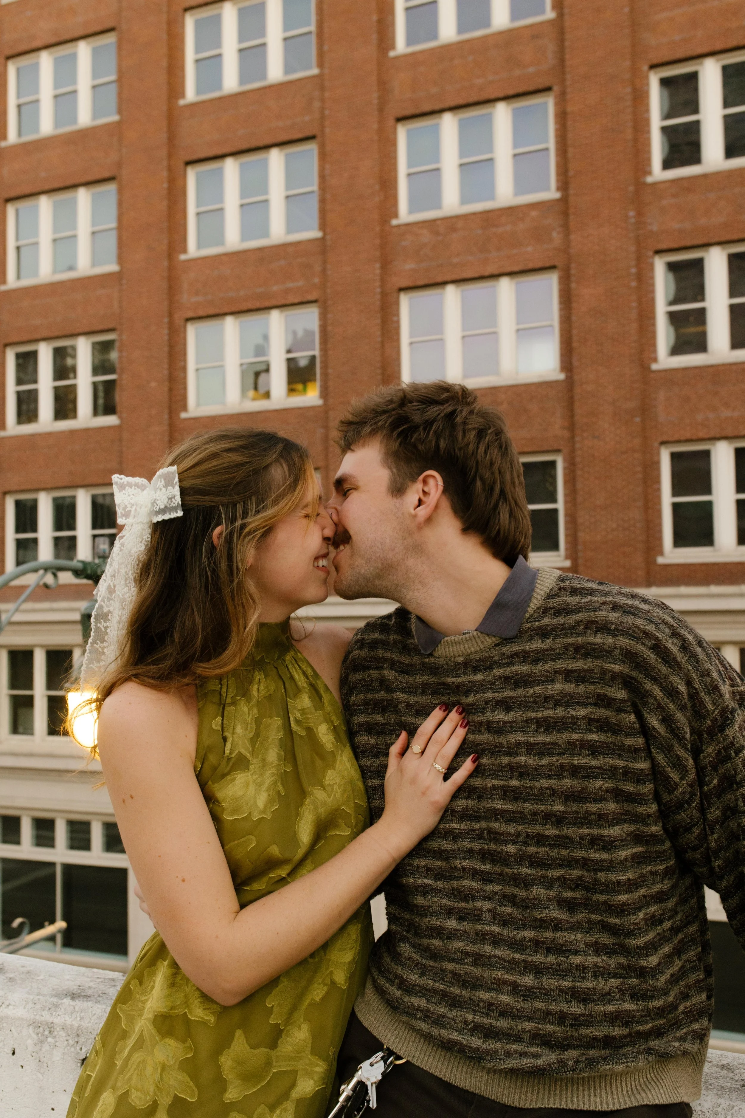 Couple leaning in for a kiss during engagement photos in NYC, with a red brick building behind them.