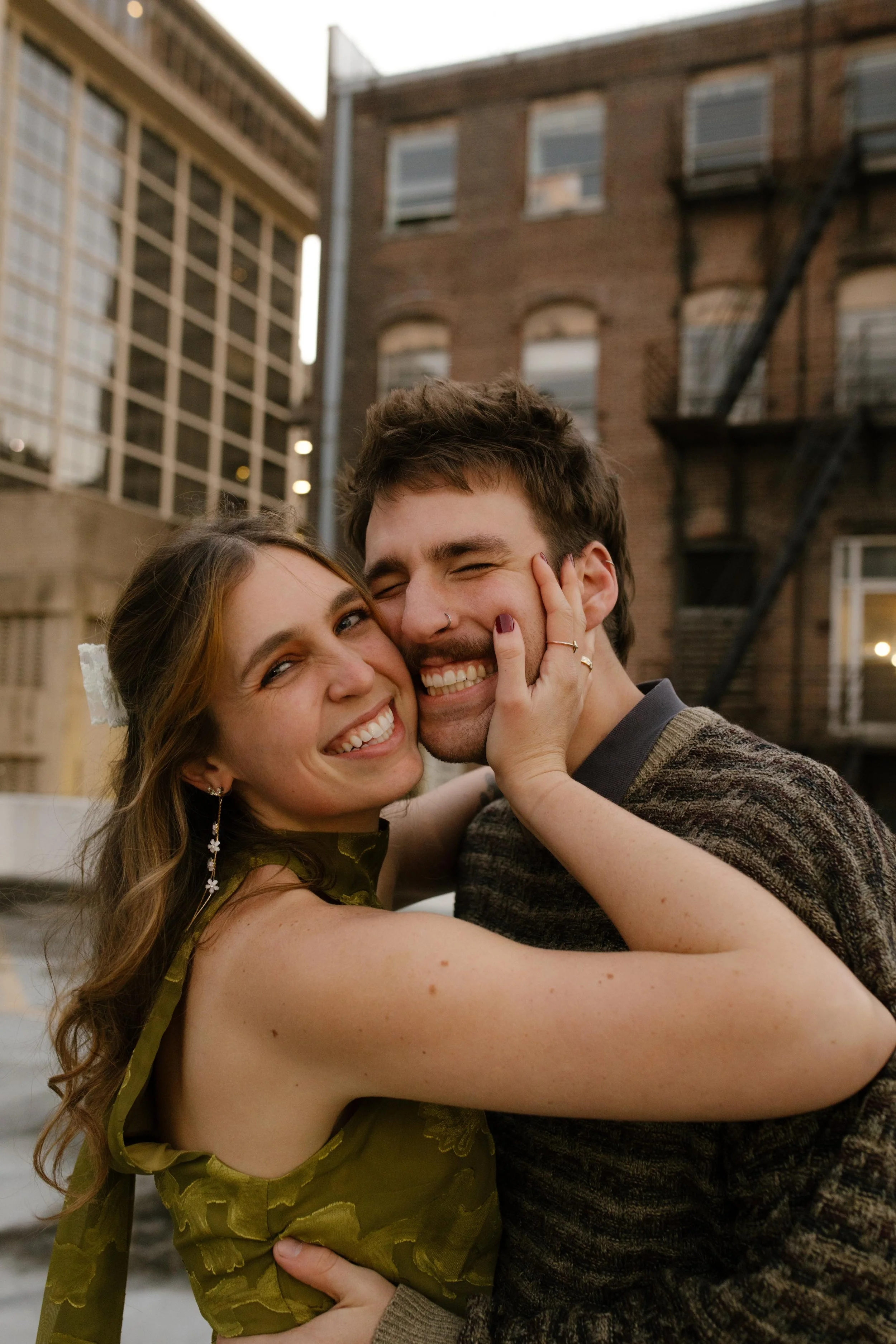 Close-up portrait of an engaged couple smiling and embracing during a playful rooftop photo session.