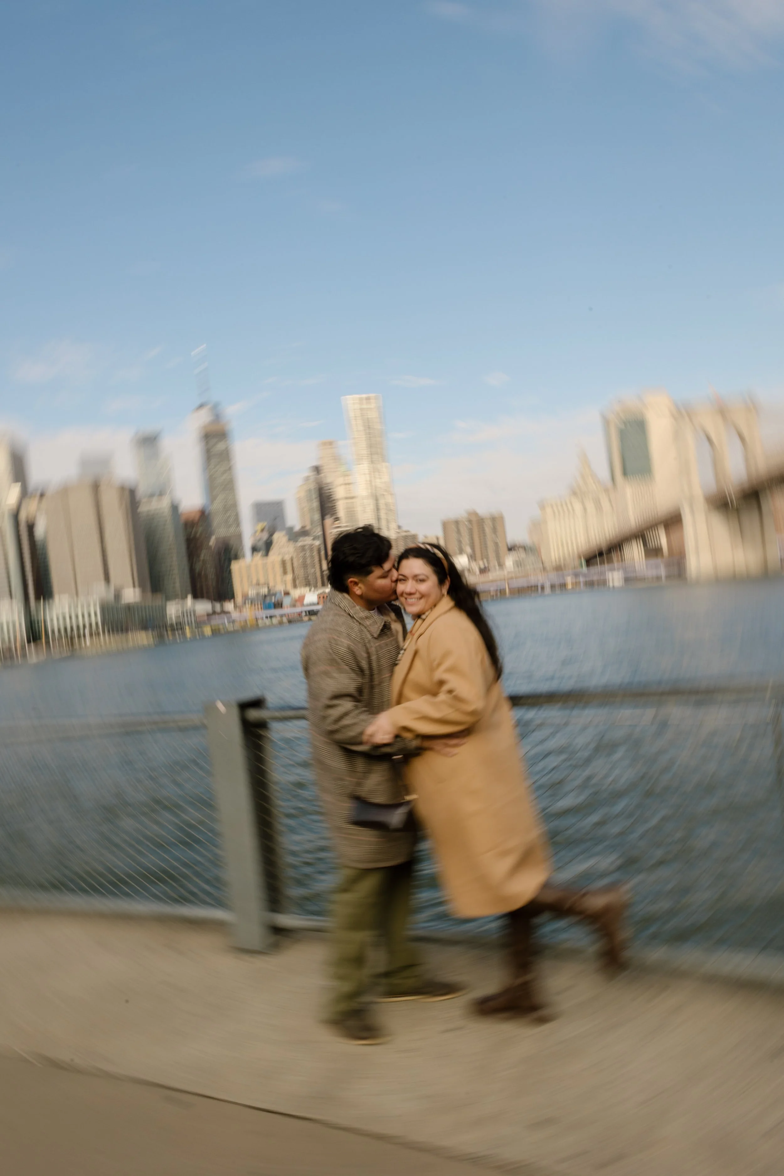 1. Creative motion blur engagement photo of a couple embracing along the Brooklyn waterfront with the city skyline behind them.