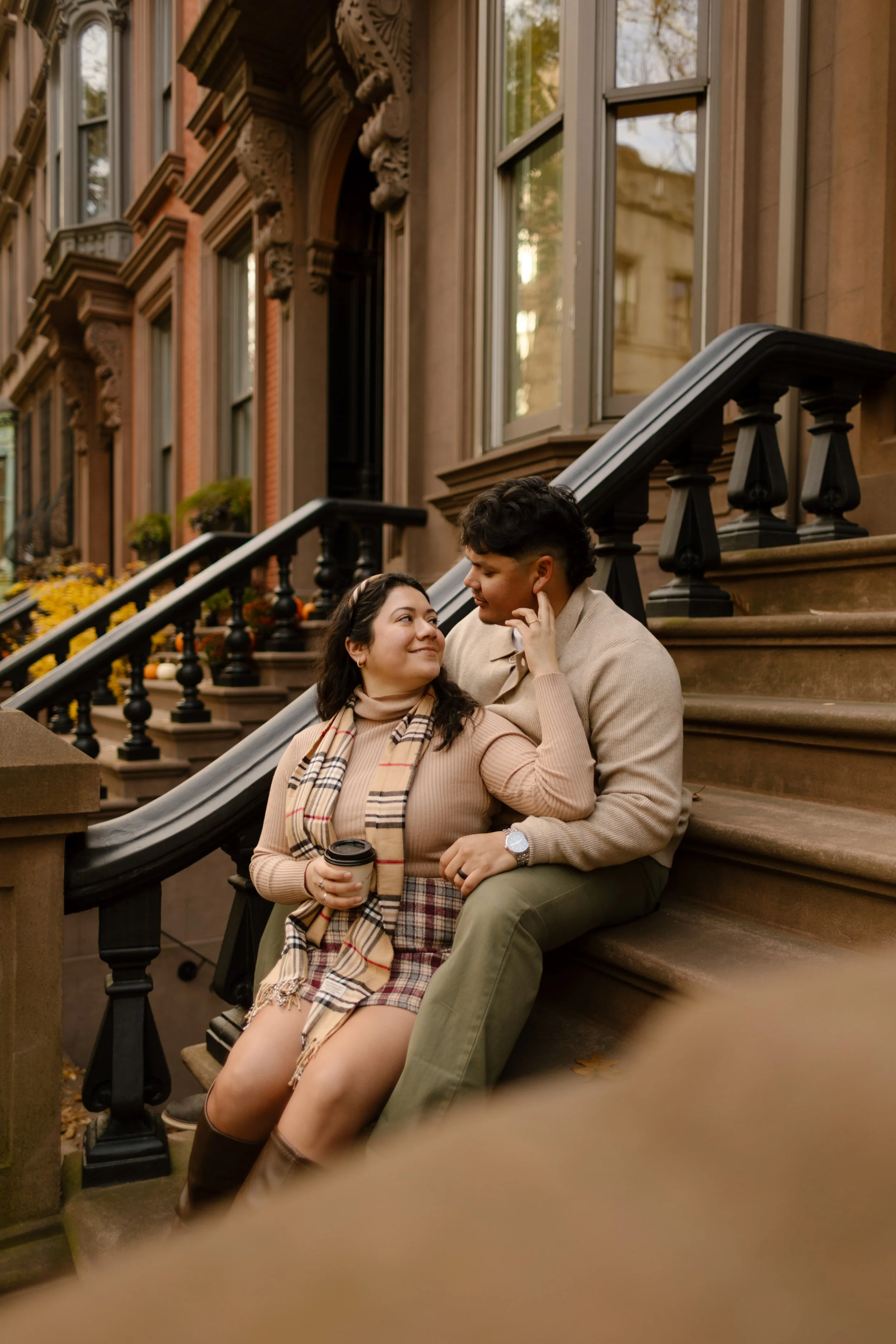 Couple cuddling on a Brooklyn Heights brownstone stoop with coffee during a cozy fall engagement session.