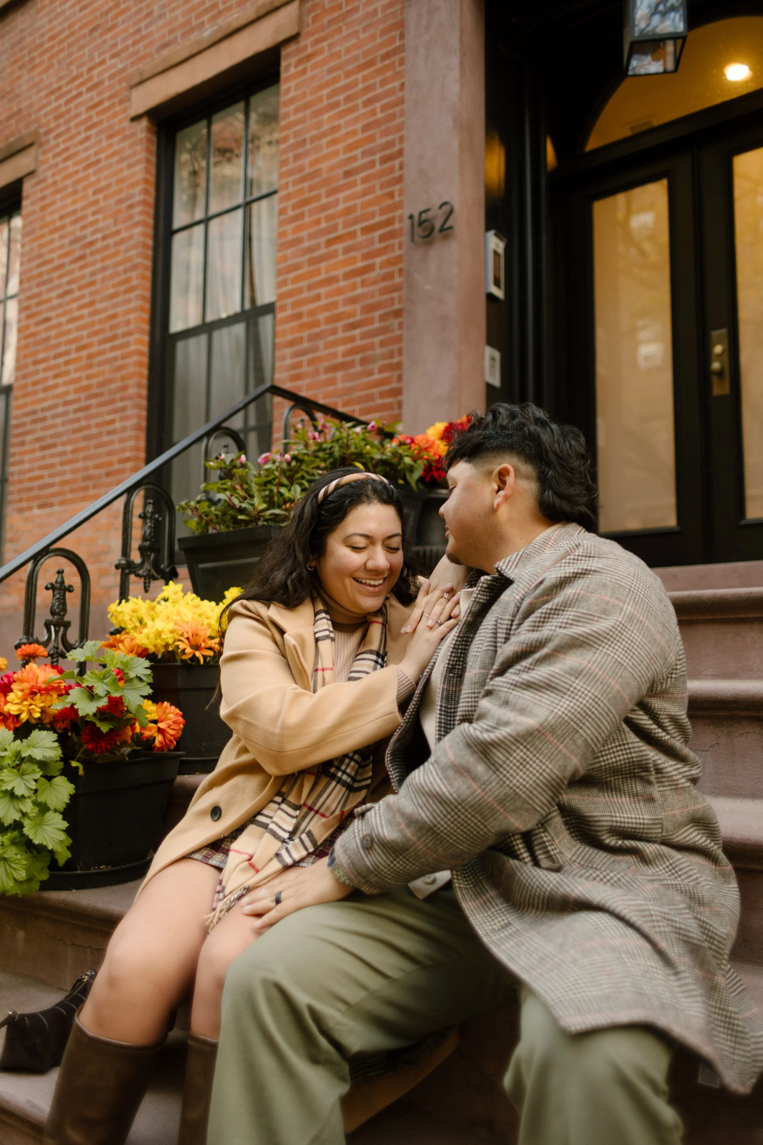 Couple laughing together on a Brooklyn brownstone stoop surrounded by colorful fall flowers.