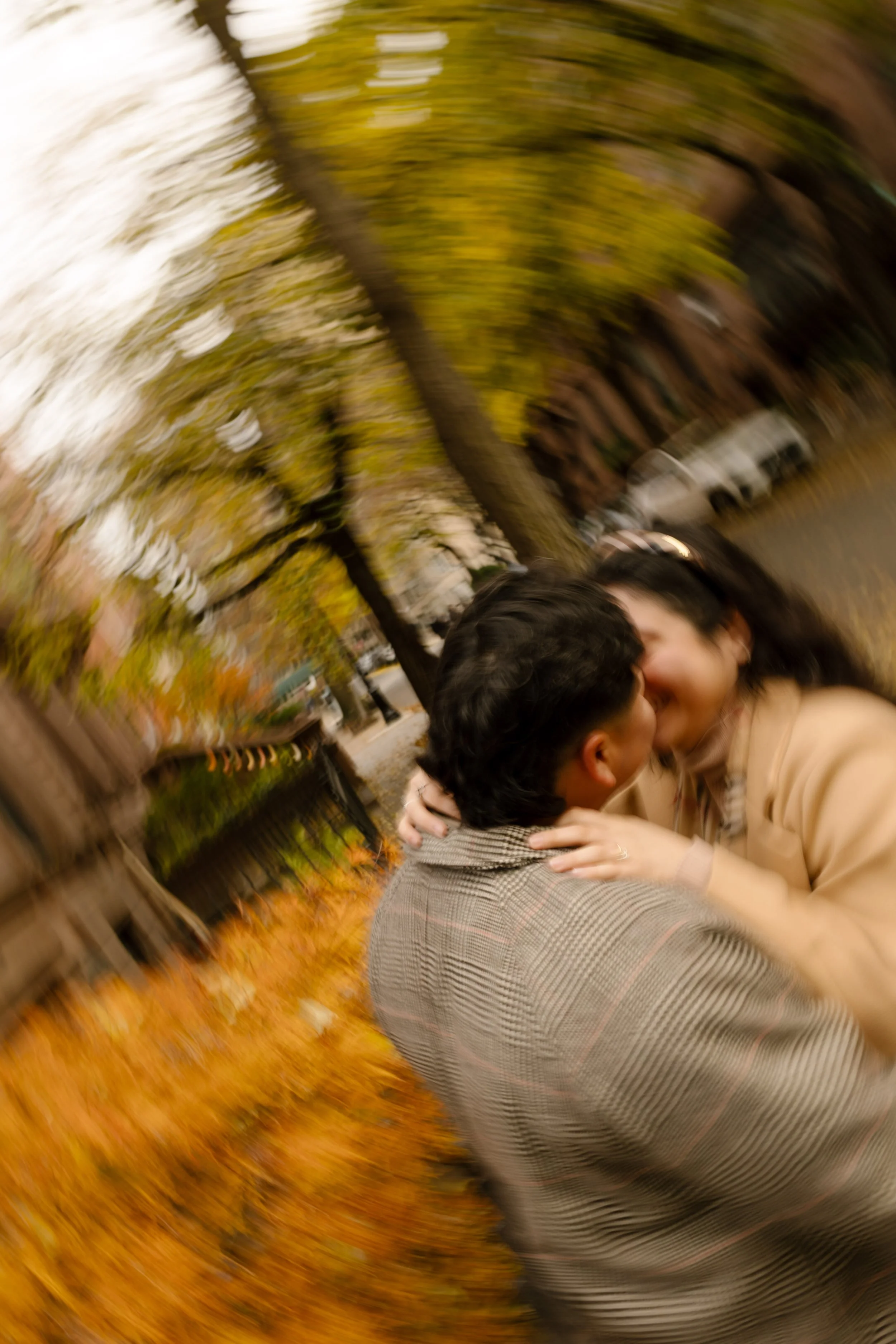 Brooklyn engagement photos with creative motion blur as a couple kisses on a tree-lined street surrounded by autumn foliage.