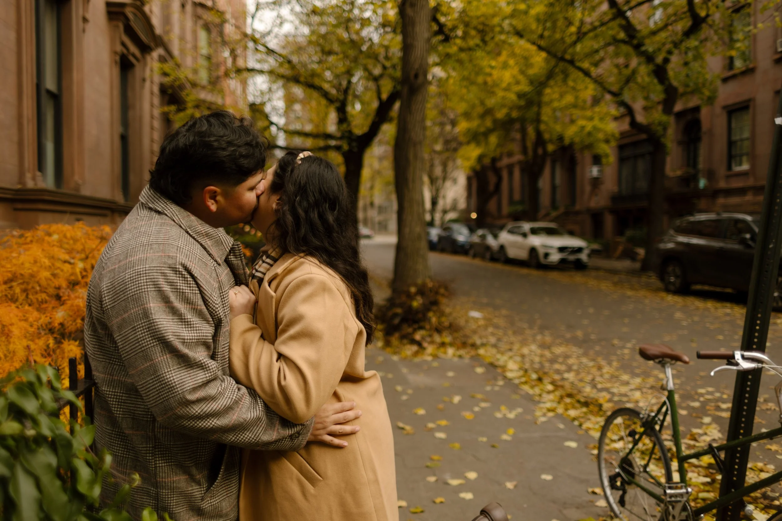 1. Couple kissing on a quiet Brooklyn Heights sidewalk surrounded by autumn leaves, brownstones, and a parked bicycle.