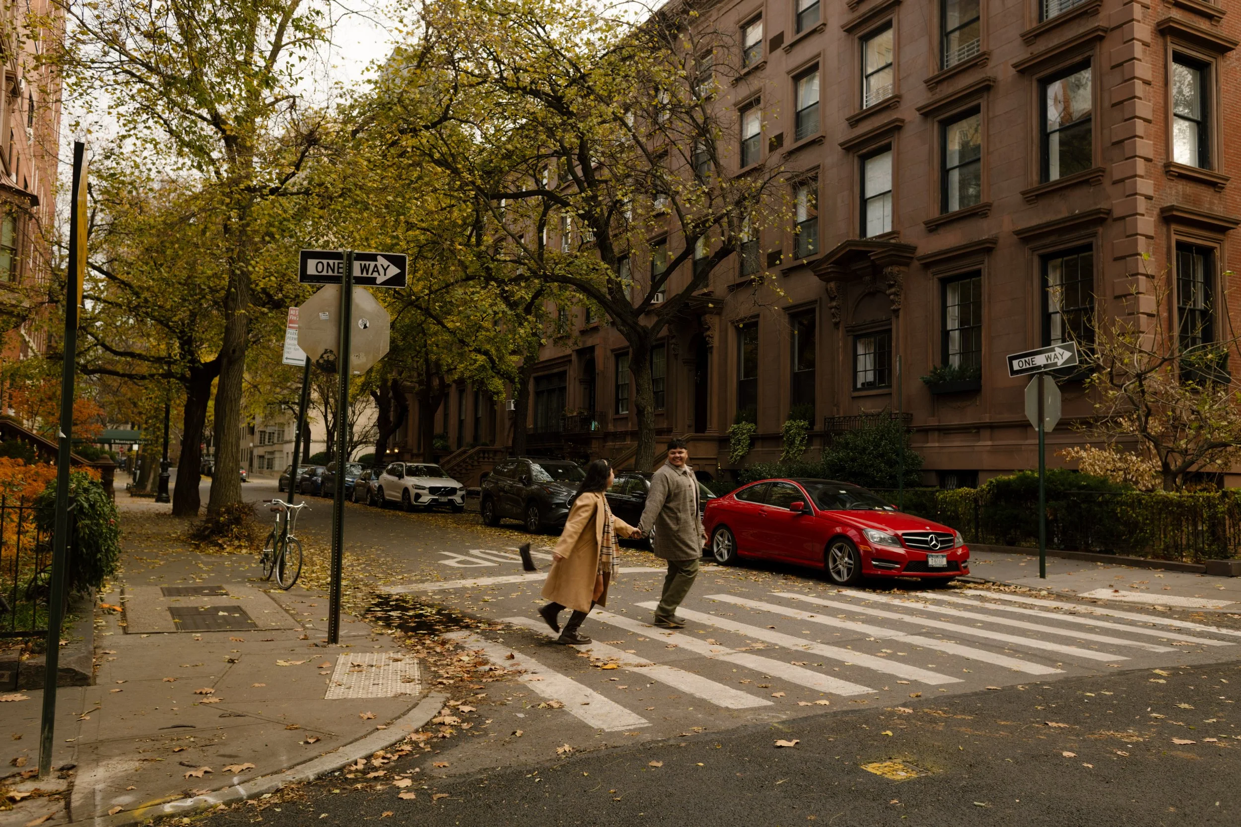 Brooklyn engagement photos of a couple running hand in hand across a brownstone-lined street during fall.