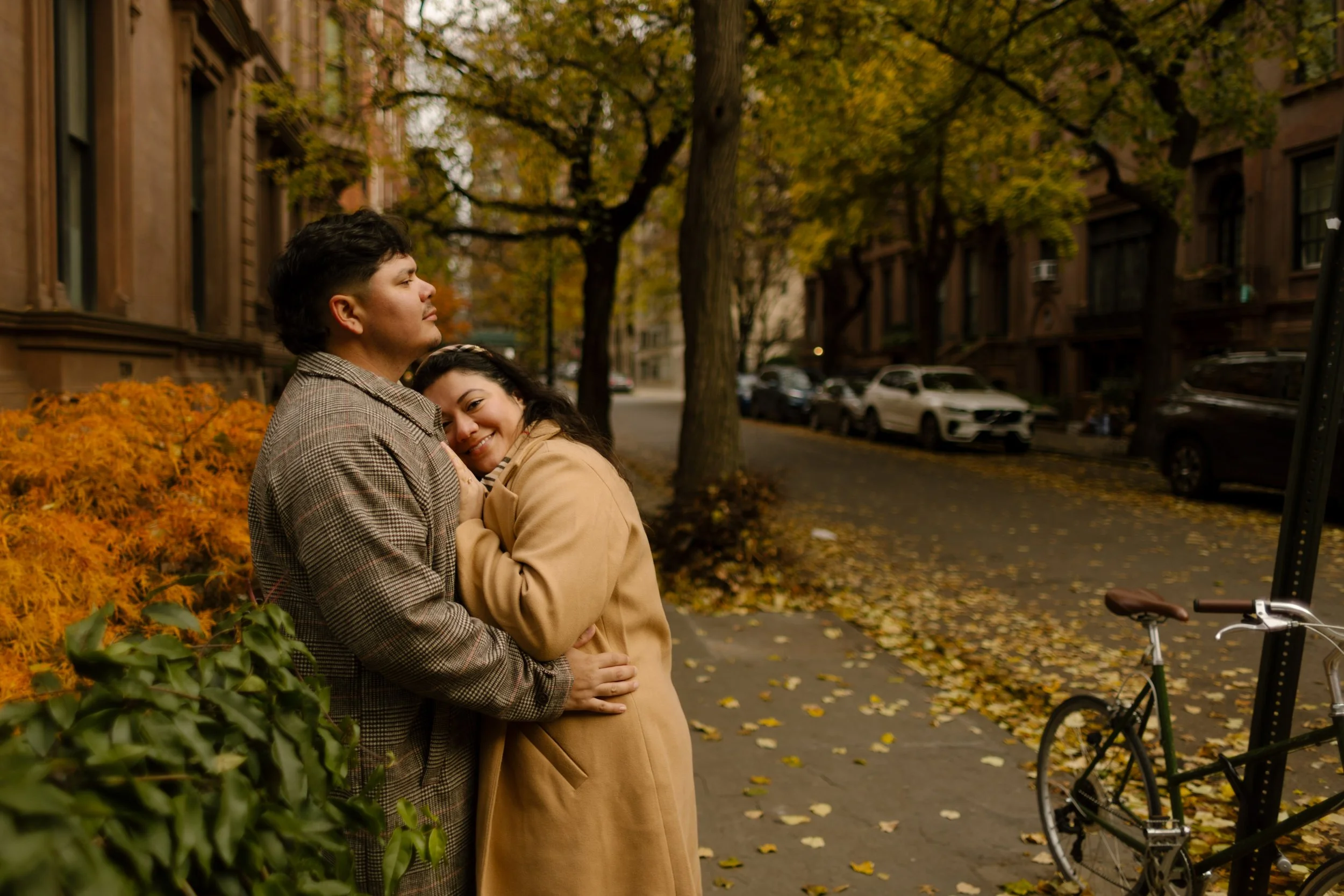 Couple cuddling on a tree-lined Brooklyn Heights street surrounded by fallen leaves and historic brownstones.