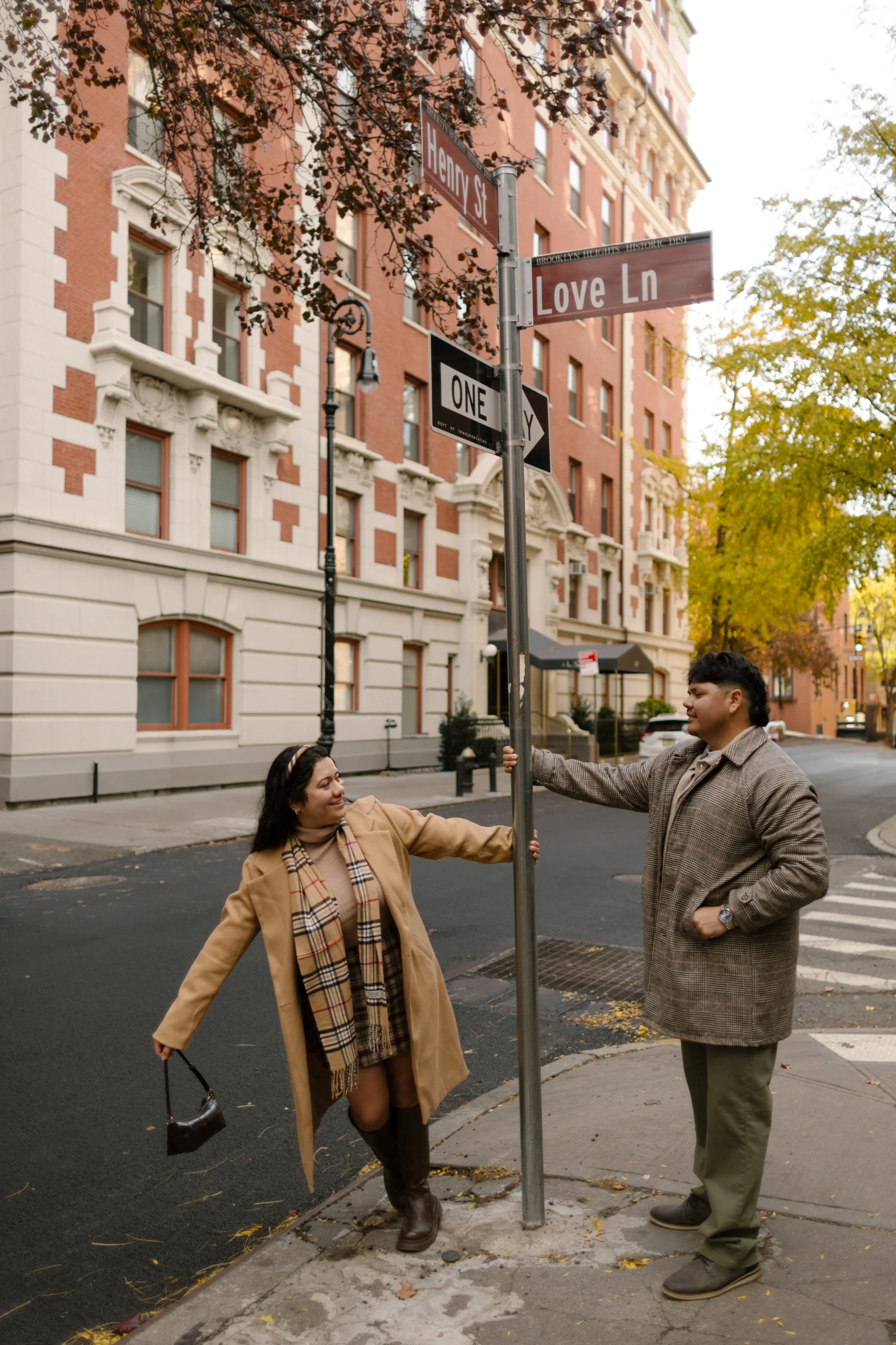 Brooklyn engagement photos of a couple playing beneath the Love Lane street sign in Brooklyn Heights during fall.