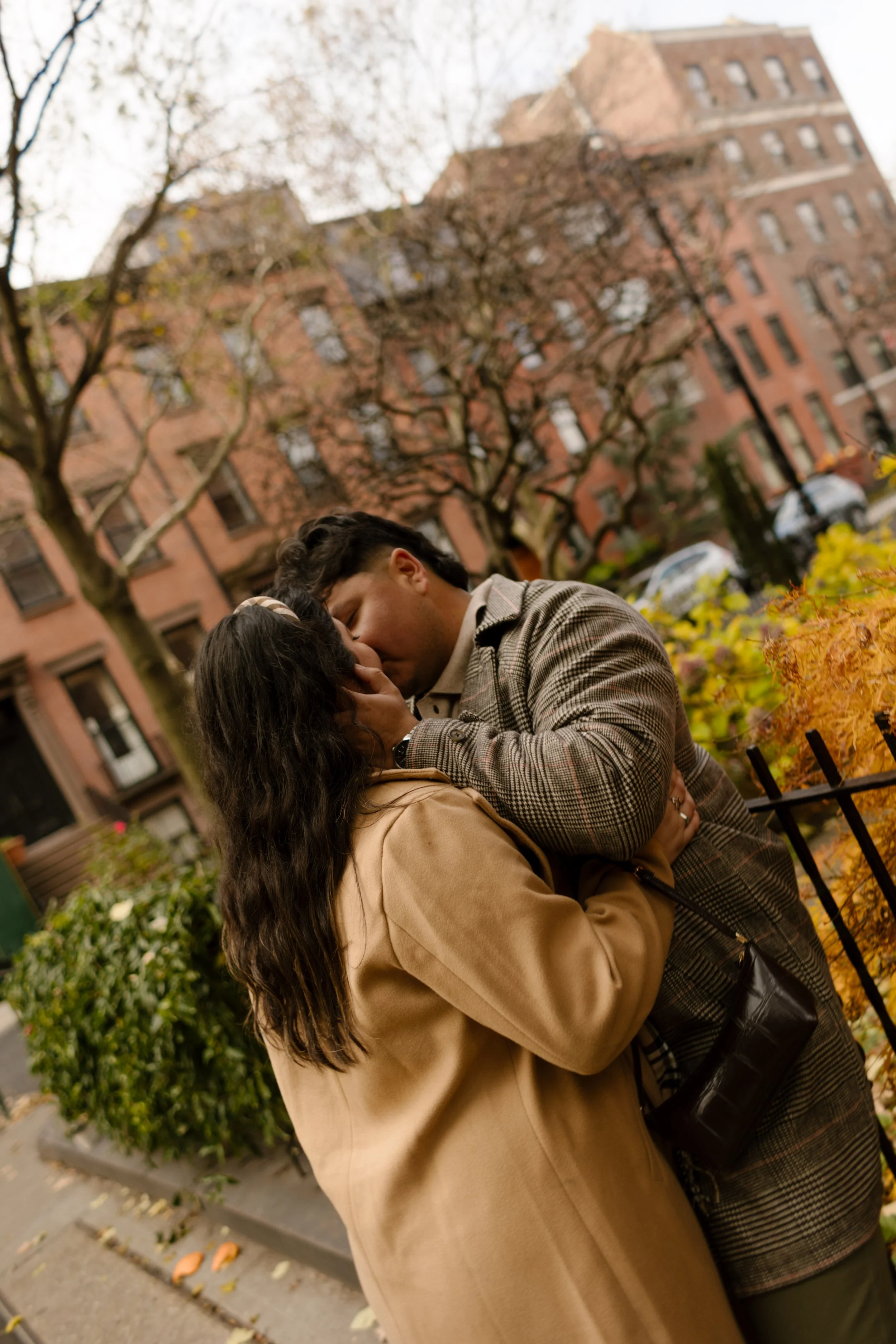 Couple kissing on a Brooklyn Heights sidewalk surrounded by brownstones and autumn foliage during their fall engagement session.