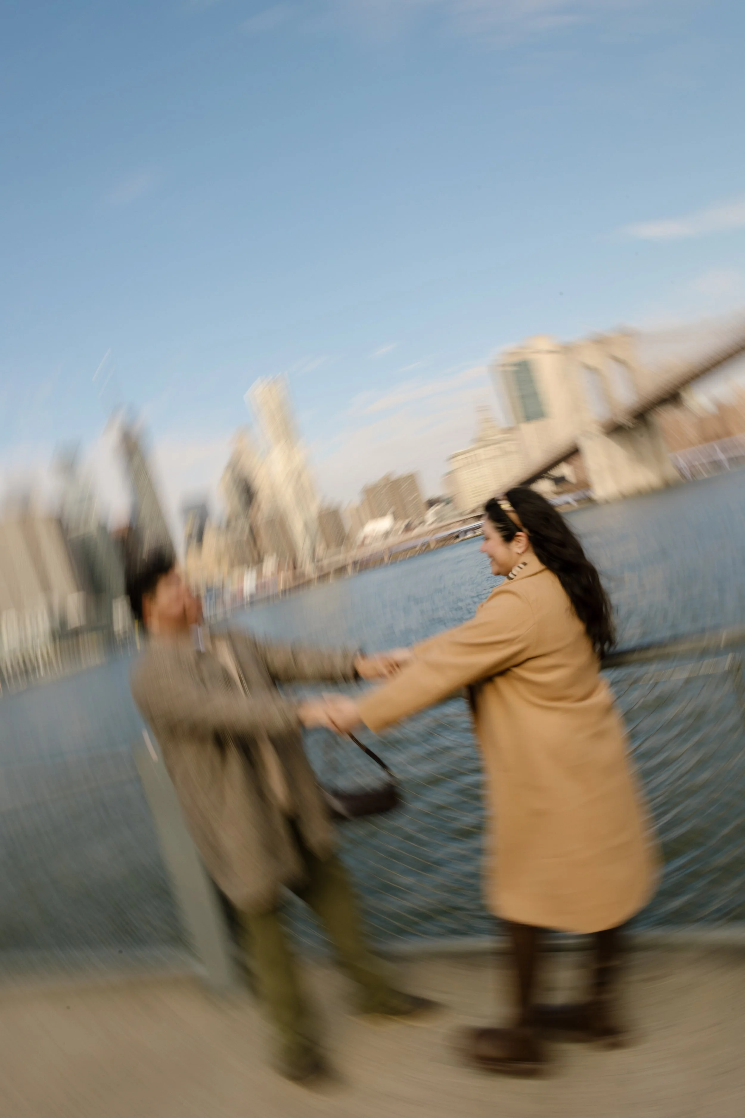 Brooklyn engagement photos with intentional motion blur as a couple holds hands along the waterfront near the Brooklyn Bridge.