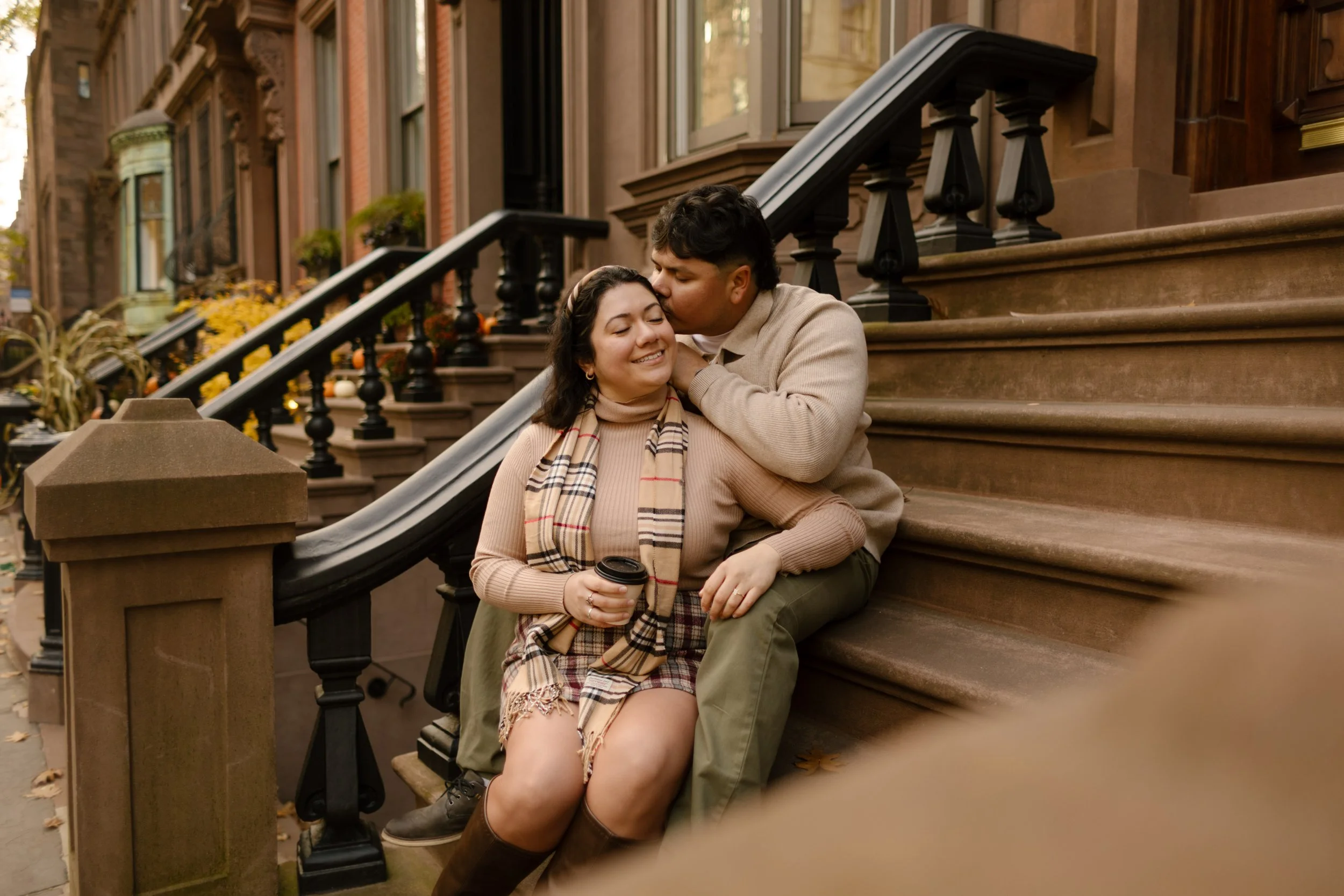 Couple cuddling on a Brooklyn brownstone stoop with coffee during a cozy fall engagement session.