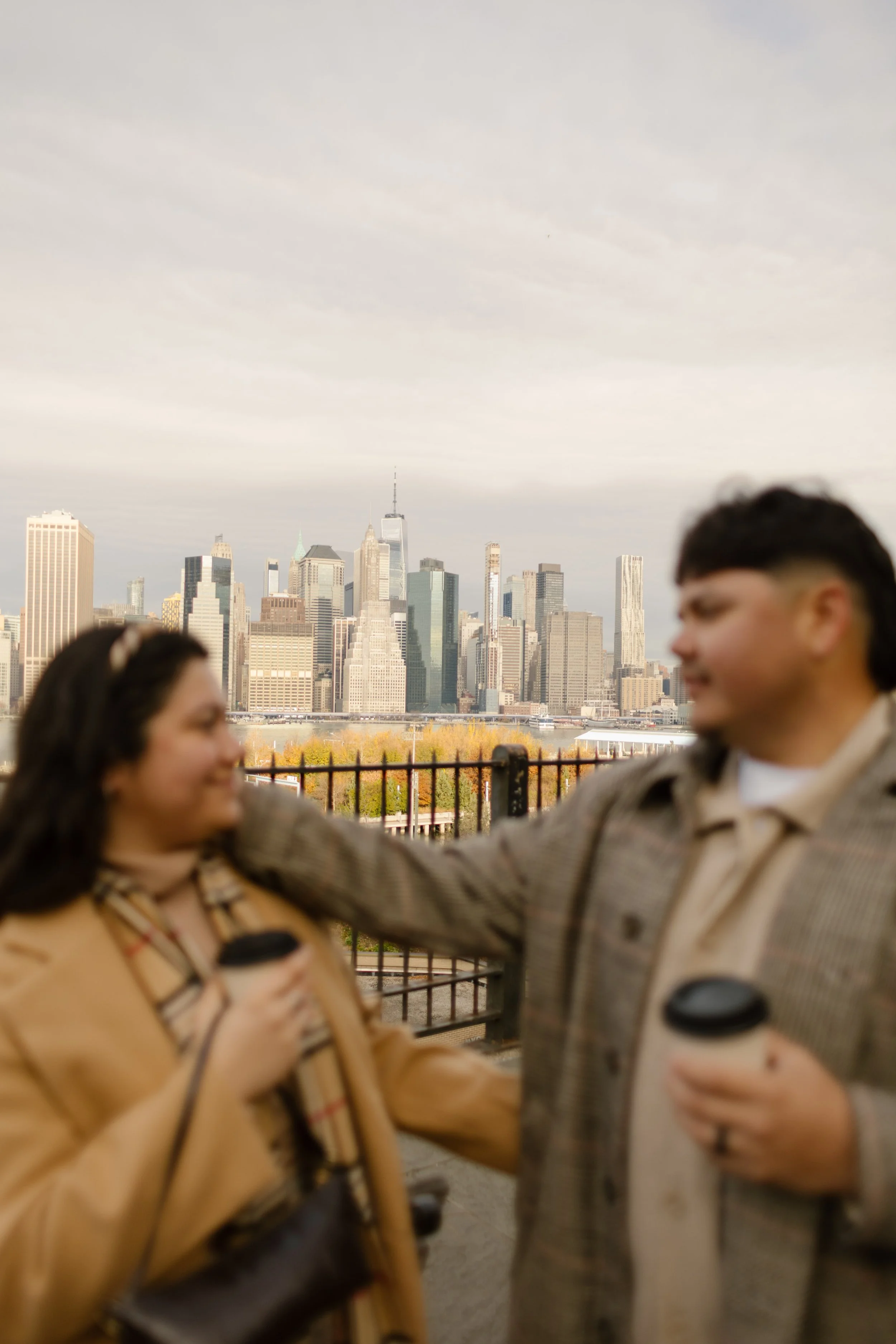 Creative picture of couple embracing while drinking coffee with Manhattan skyline behind them. 