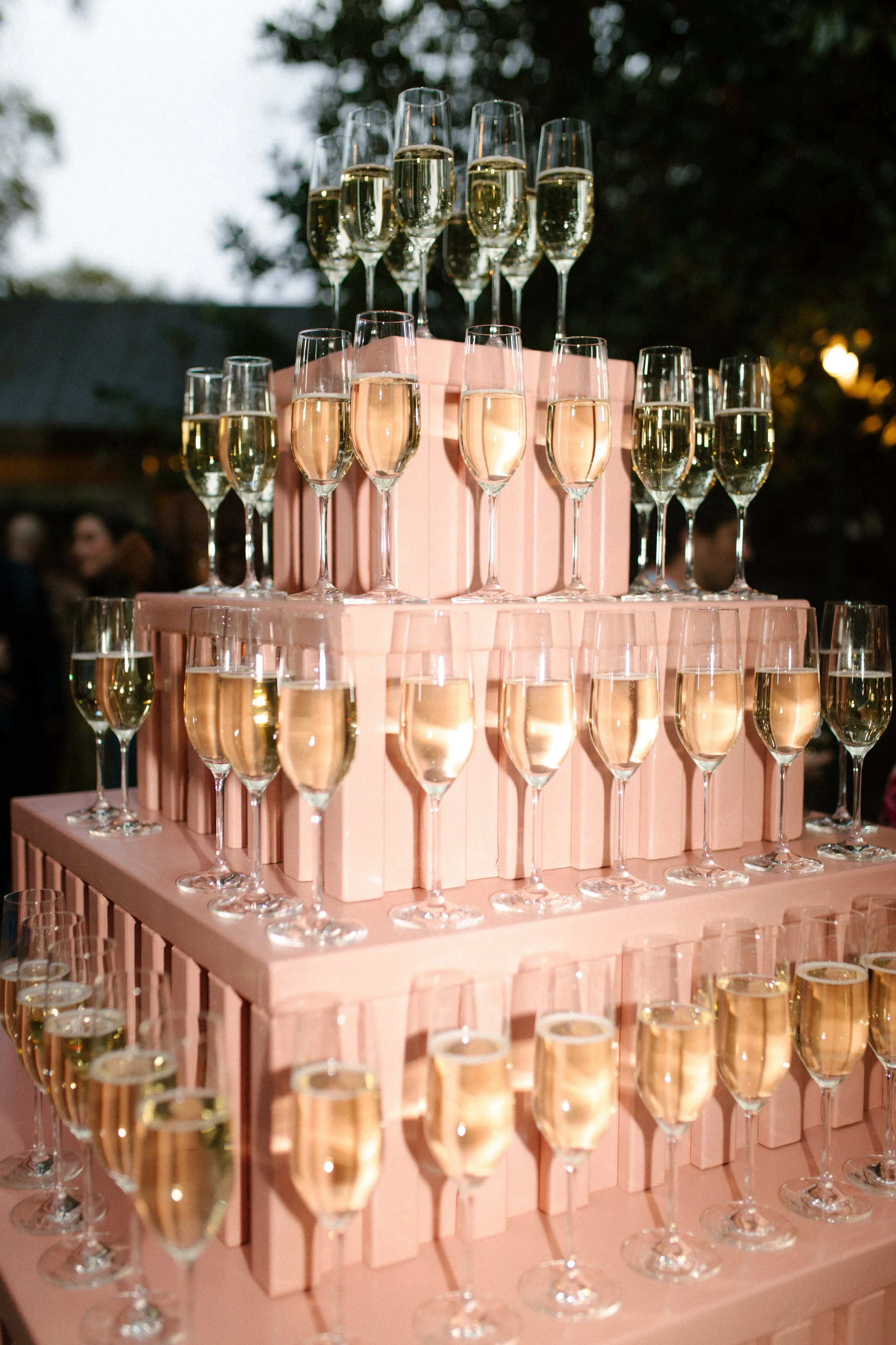 Champagne tower display with pink tiers and filled glasses at an elegant outdoor wedding reception.