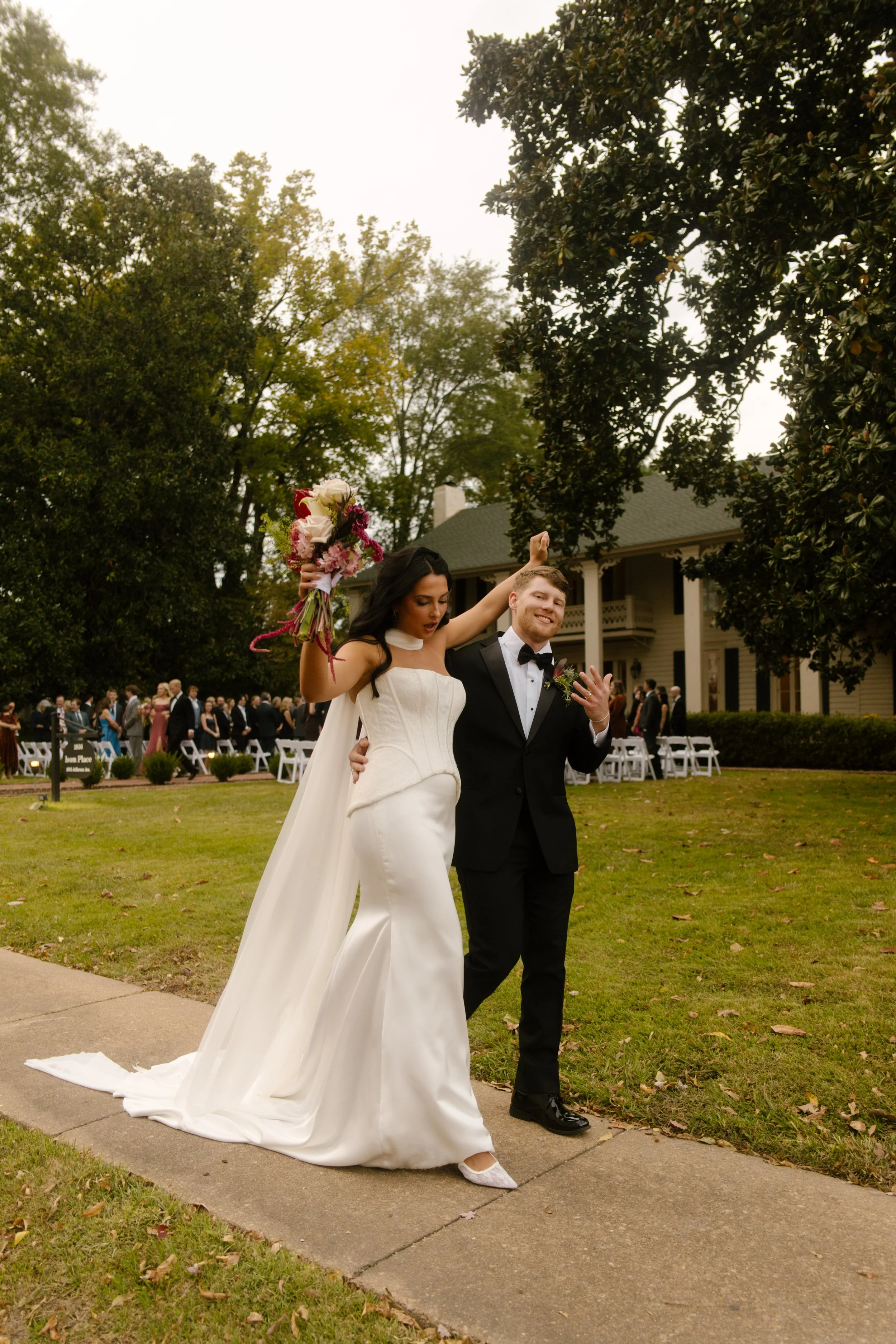 Bride and groom celebrating outdoors with a colorful bridal bouquet, black tuxedo, and moody wedding colors.