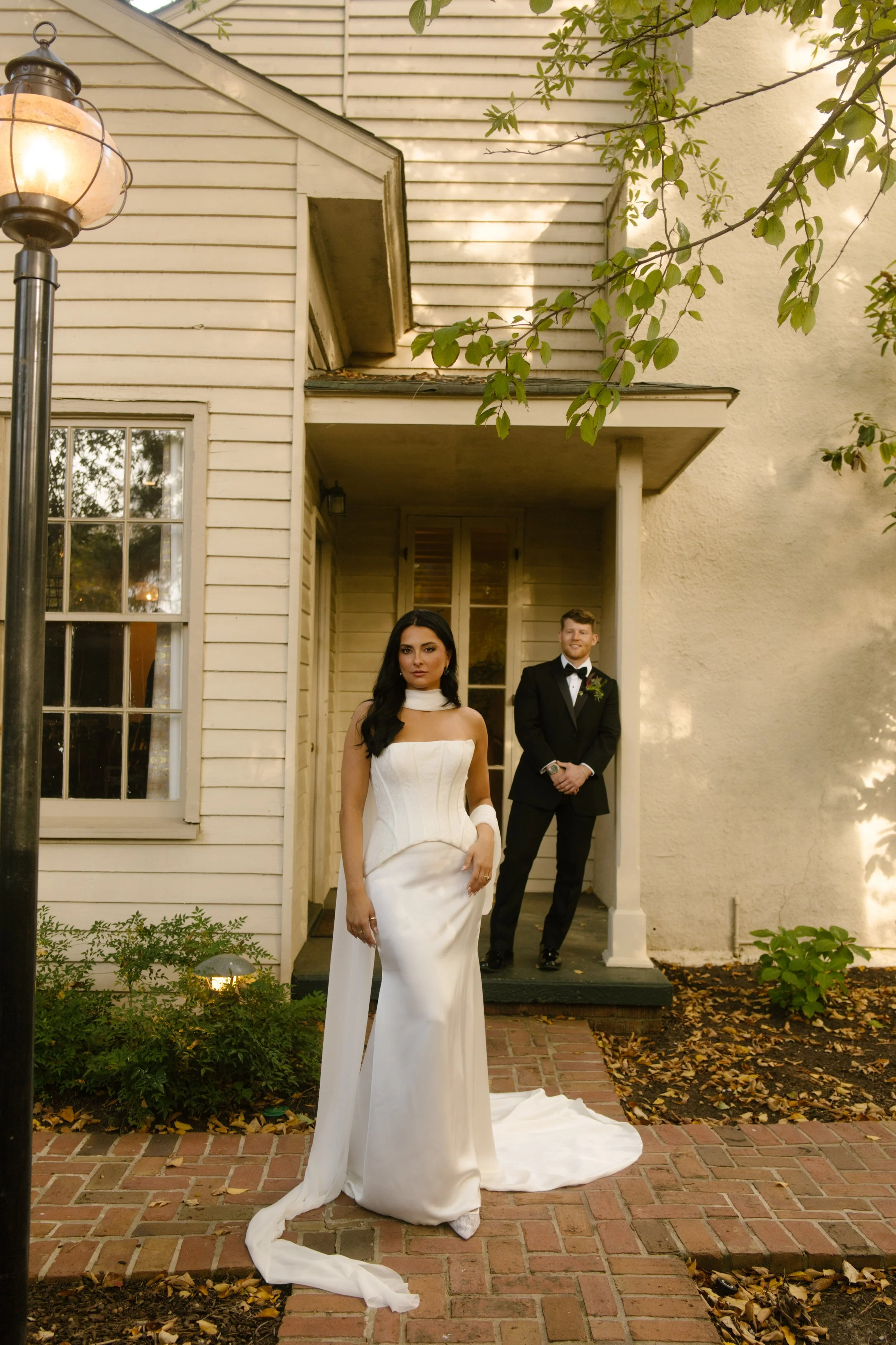Editorial wedding portraits of a bride in a white gown and groom in a black tuxedo outside a historic building.