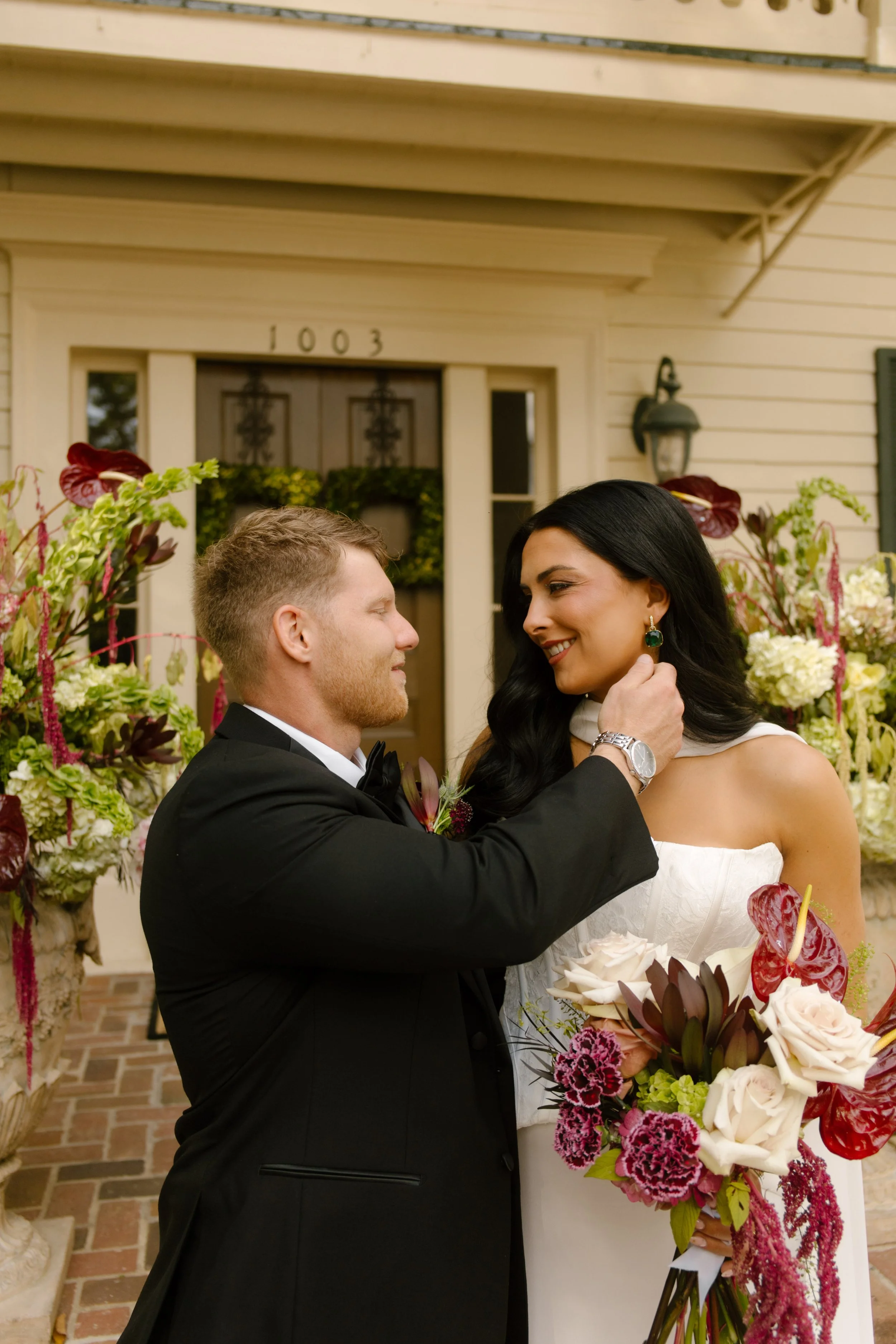 Bride and groom sharing a romantic moment beside floral arrangements featuring moody wedding colors of burgundy, plum, and ivory.