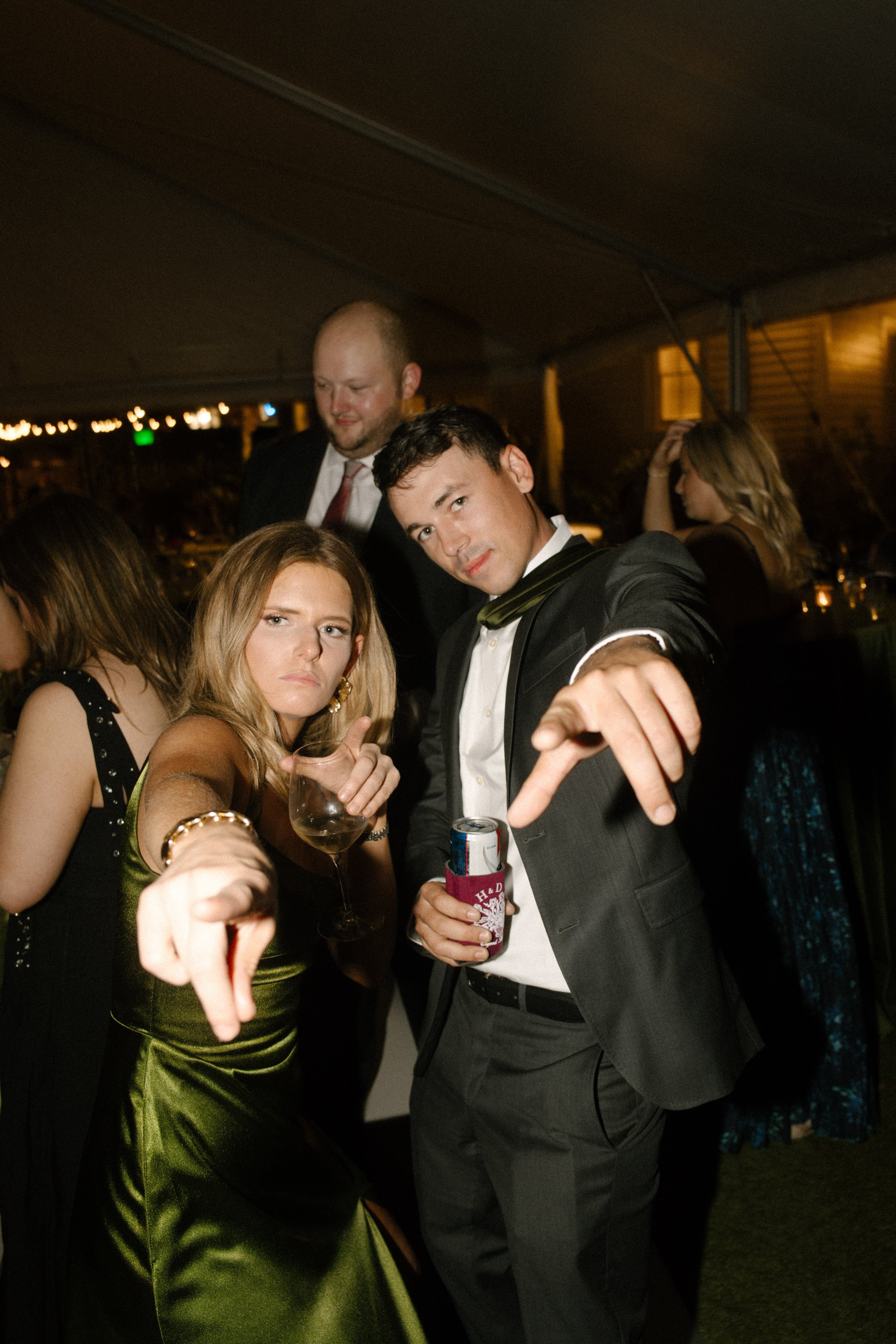 Wedding guests dancing at a nighttime reception, featuring an olive green satin dress and playful candid moments.