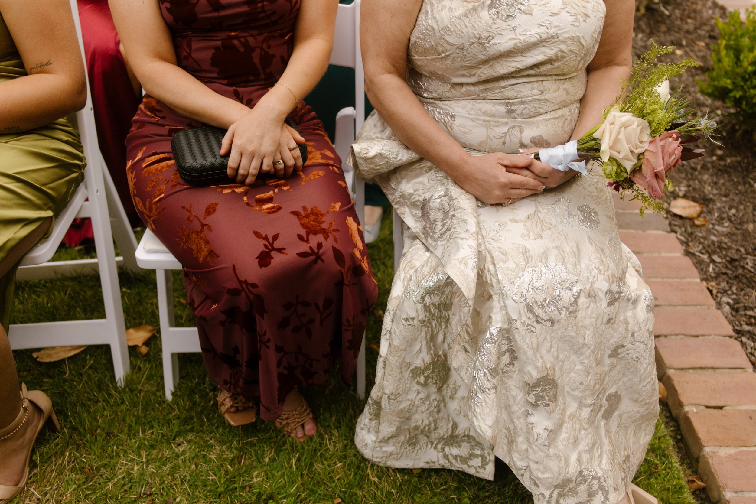 Wedding guest outfits featuring burgundy floral satin and champagne brocade dresses at an outdoor ceremony.