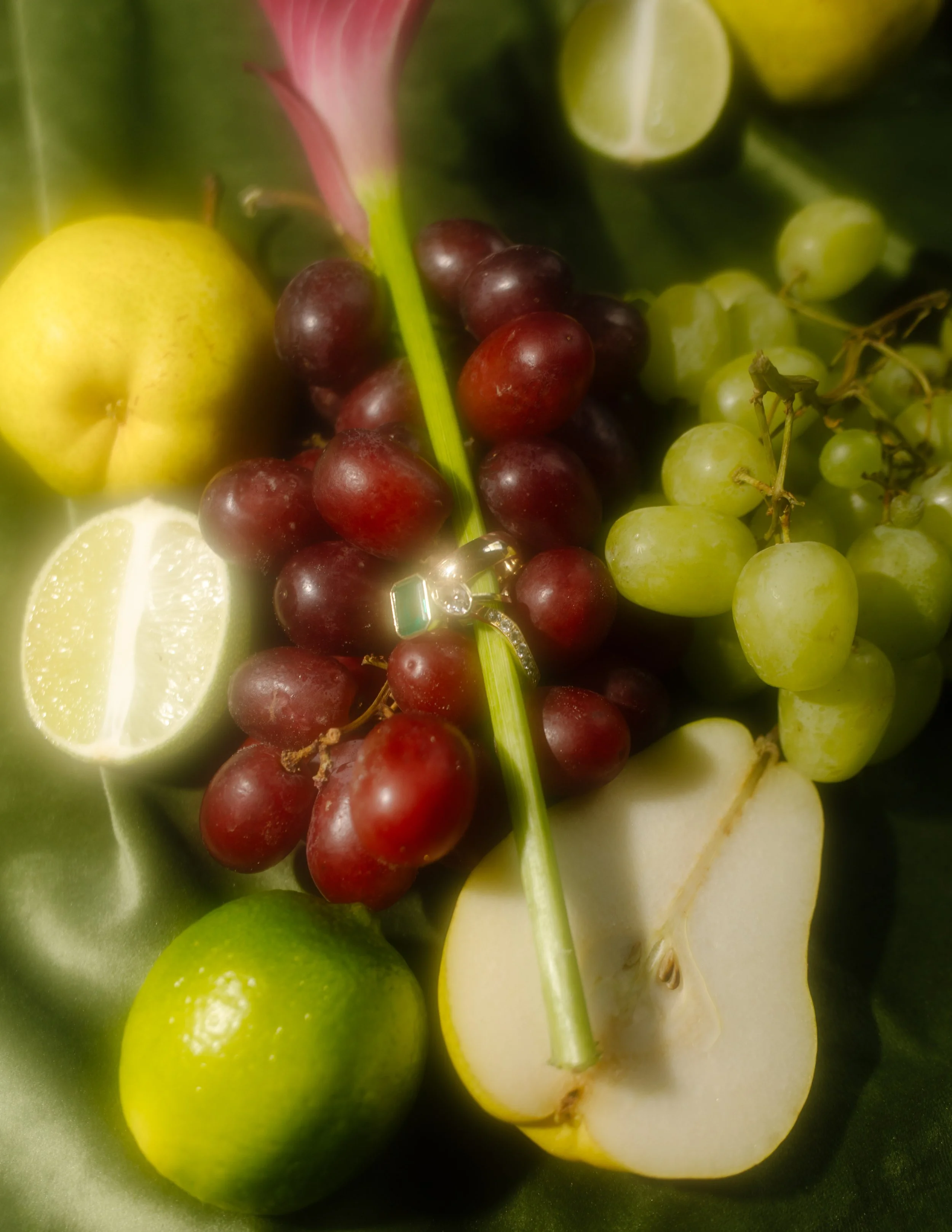 Close-up of an engagement ring among red grapes, green grapes, pears, and citrus arranged in moody wedding colors.