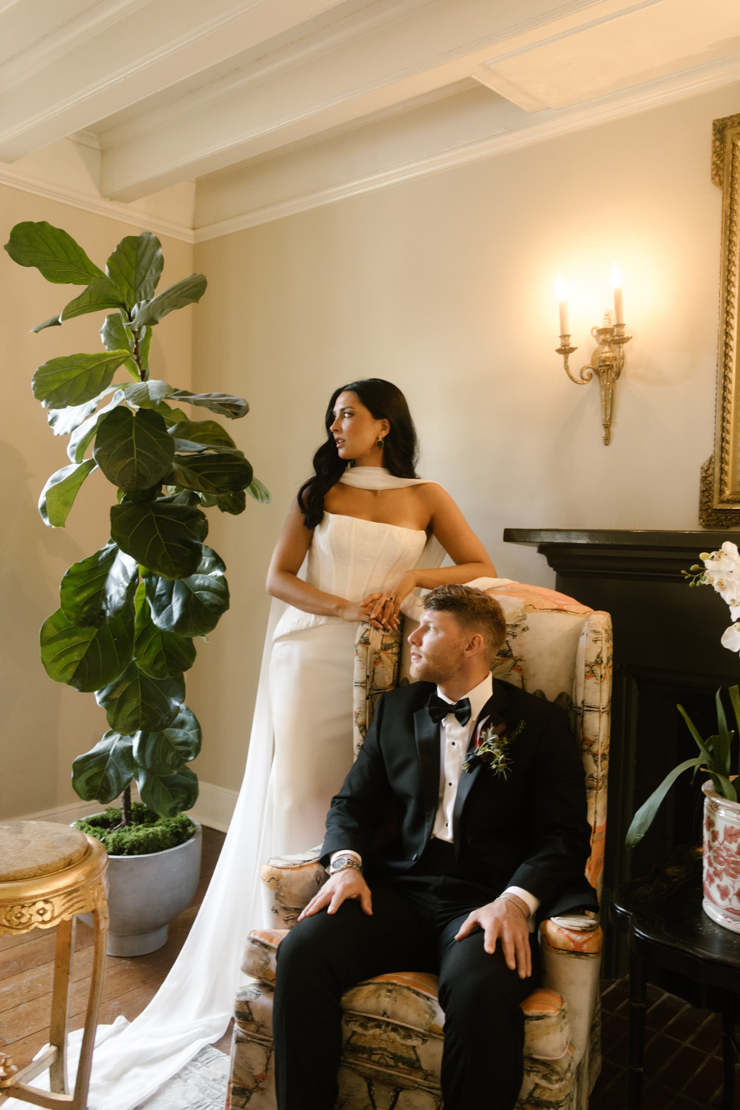 Editorial bride and groom portraits in a vintage sitting room with warm lighting, floral furniture, and moody wedding colors.