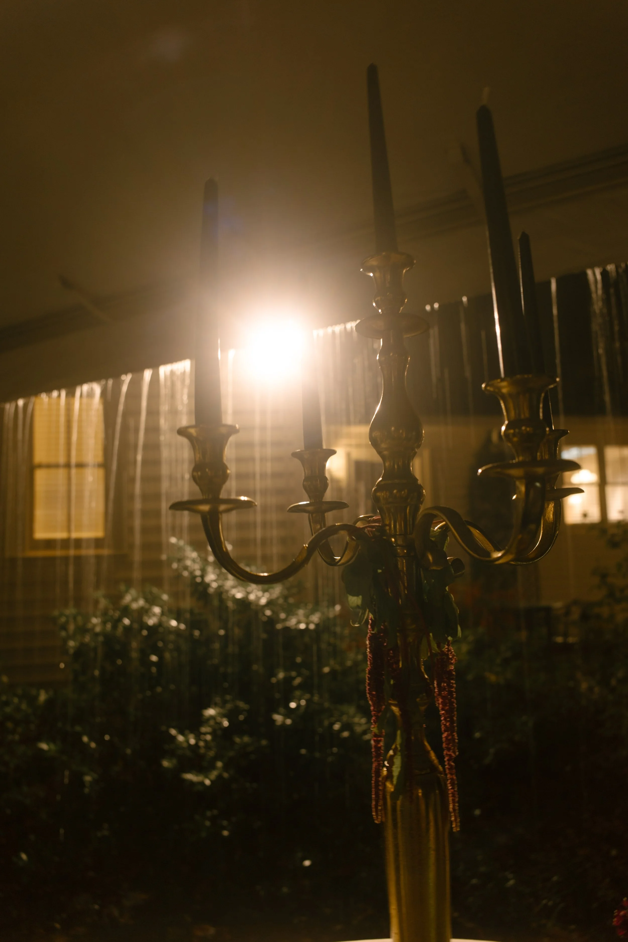 Moody wedding reception lighting with an antique brass candelabra and warm golden light inside a tent.