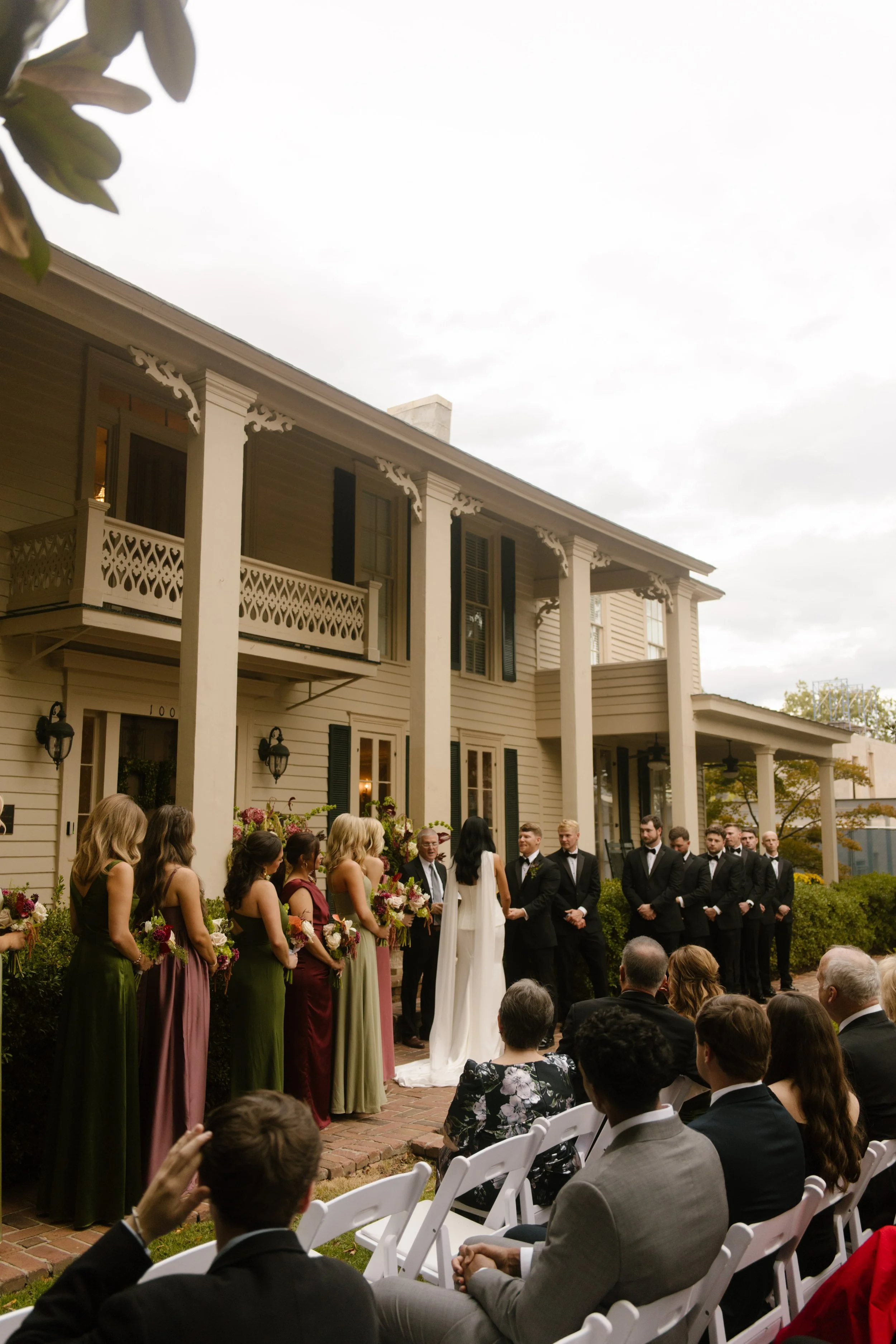 Outdoor wedding ceremony featuring moody wedding colors in burgundy and olive green bridesmaid dresses with romantic floral arrangements.