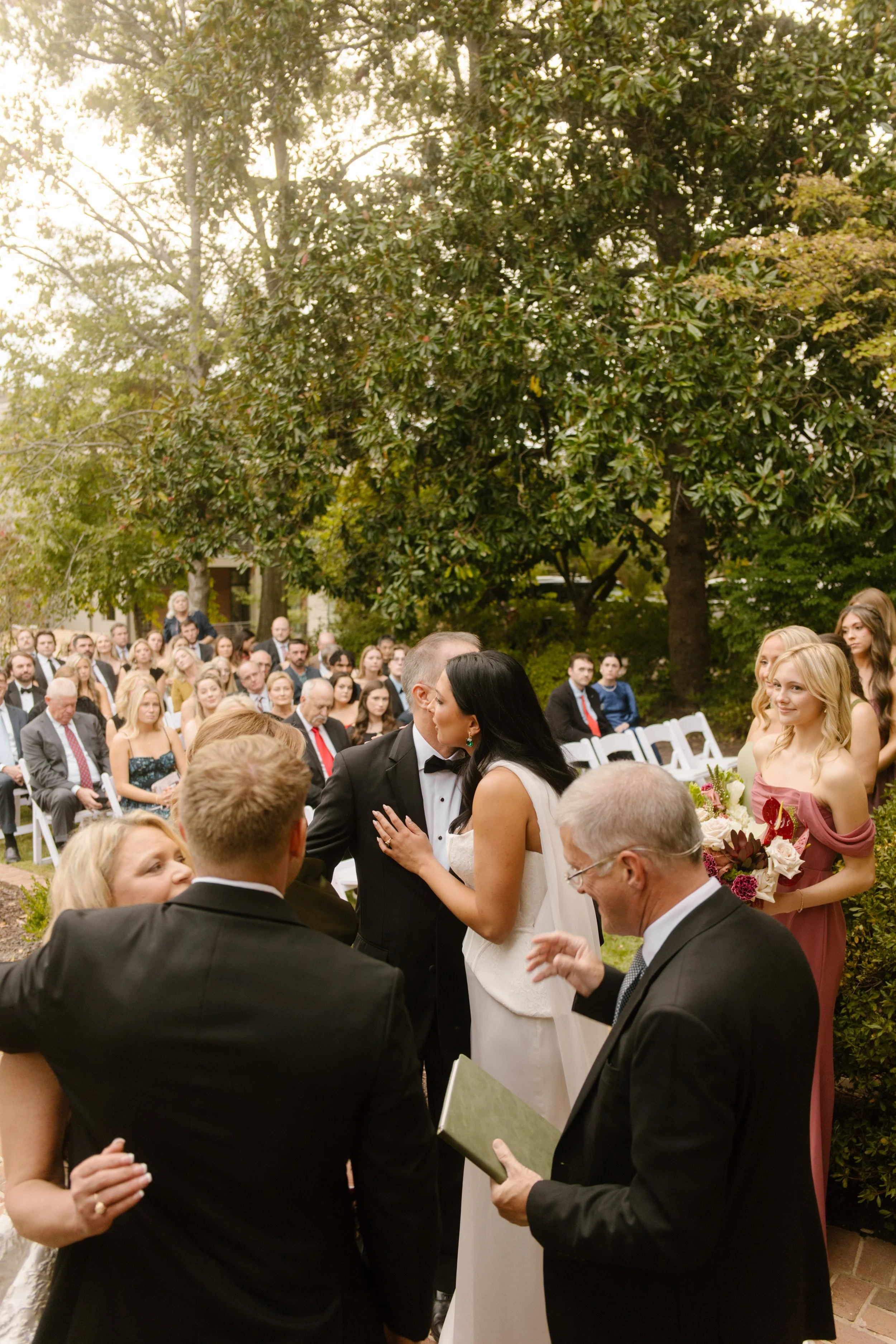 Bride and groom sharing a kiss during their outdoor wedding ceremony surrounded by family and friends.