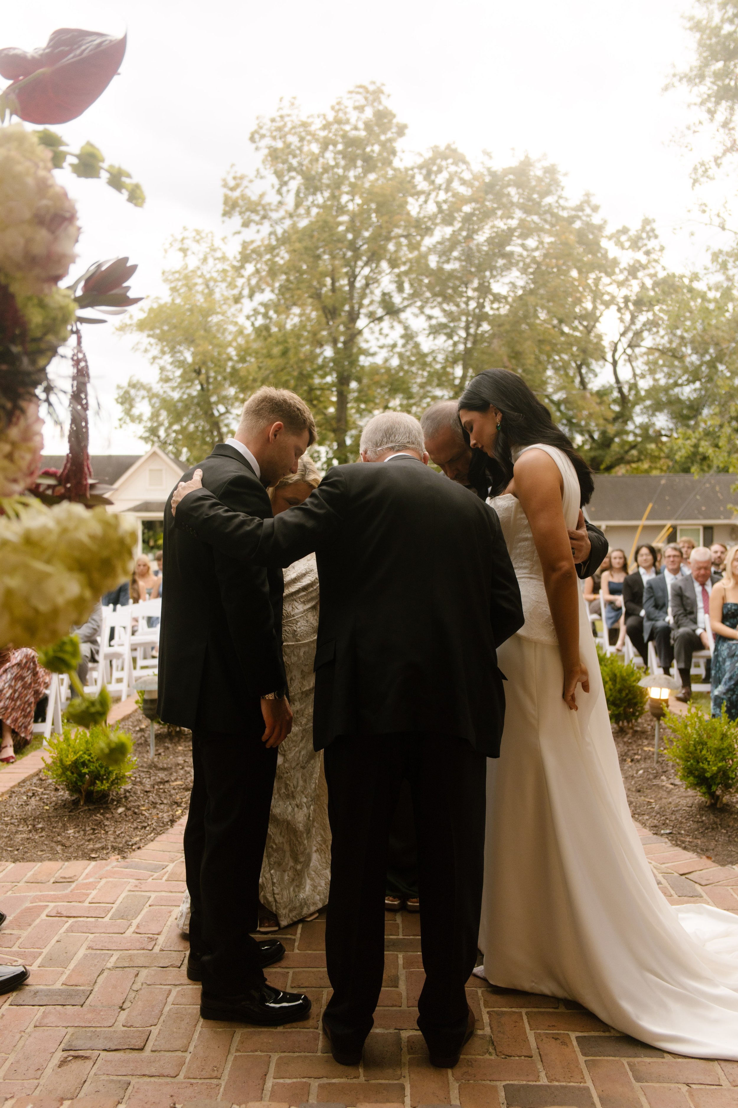 Bride and groom standing with family during an intimate outdoor wedding ceremony beneath the trees.